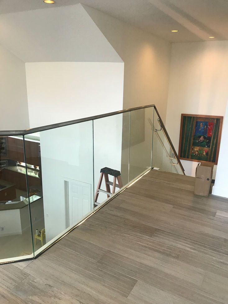 Modern home interior with glass railing and wooden floor. A-frame ladder sits near a painting.