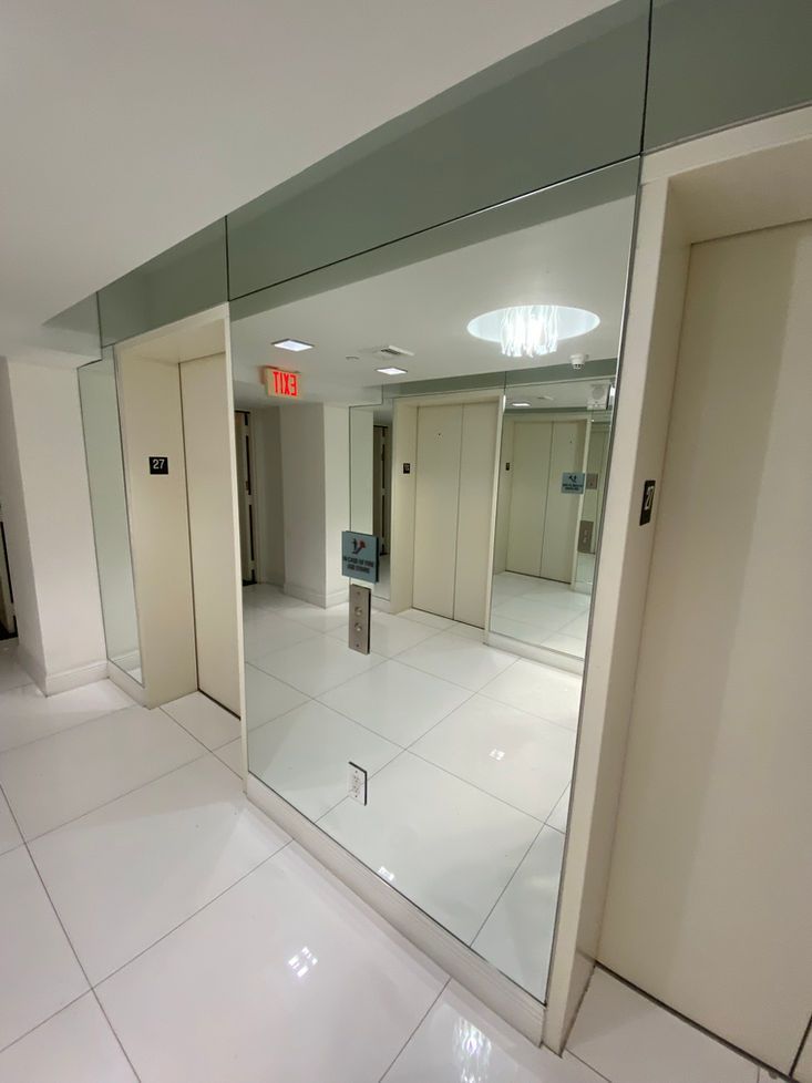 Hallway with mirrored wall and elevators. White walls, tile floor, and ceiling light.