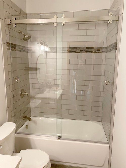 Bathroom with glass sliding shower doors, white tile walls, and a white bathtub.