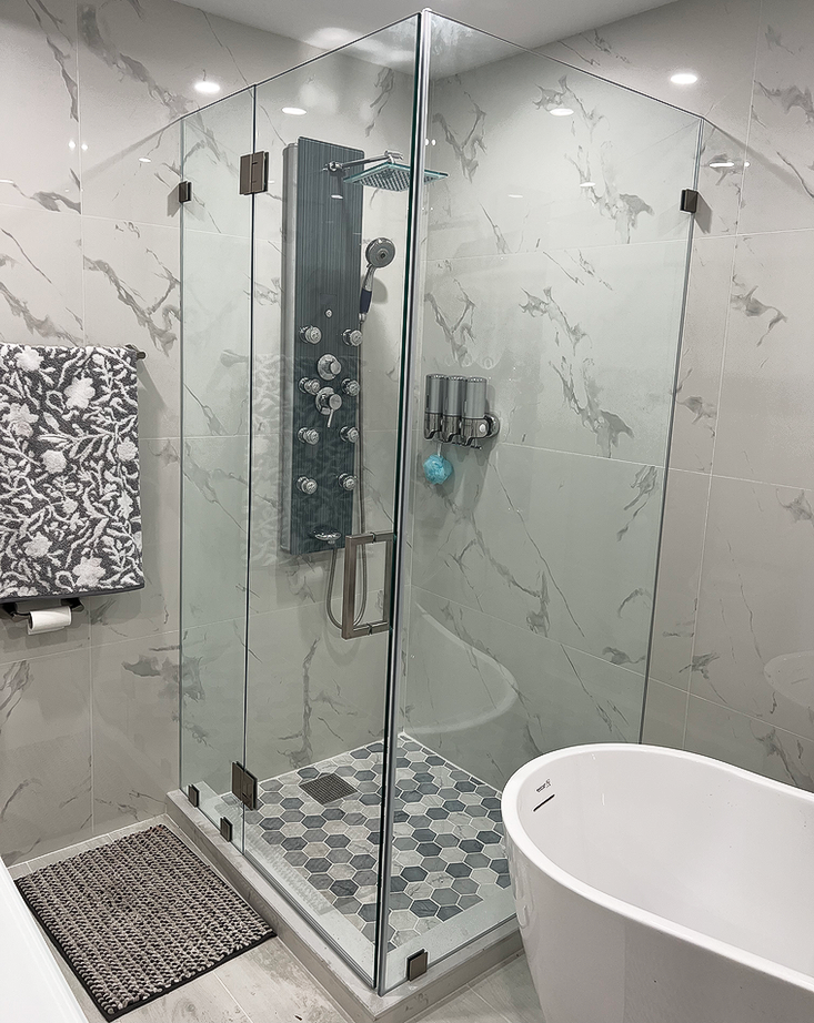 Modern bathroom with glass shower enclosure, marble-like tiles, and a freestanding tub.