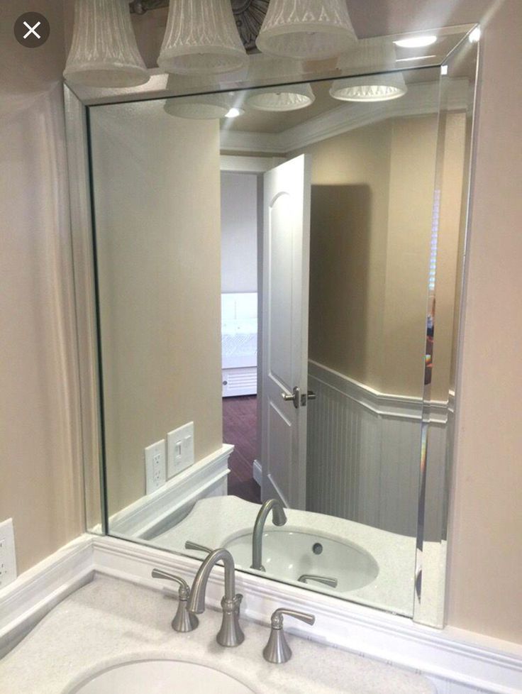 Bathroom with a large, rectangular mirror above a sink. Reflects a doorway and adjacent room.