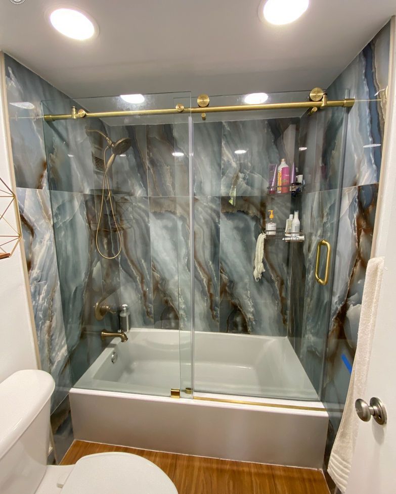 Bathroom with blue, marble-look tile, gold hardware, glass shower door over a bathtub.