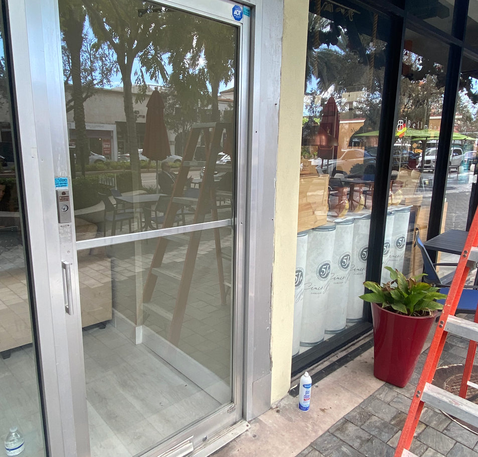 Exterior of business with glass door, window, red flower pot, and a ladder.