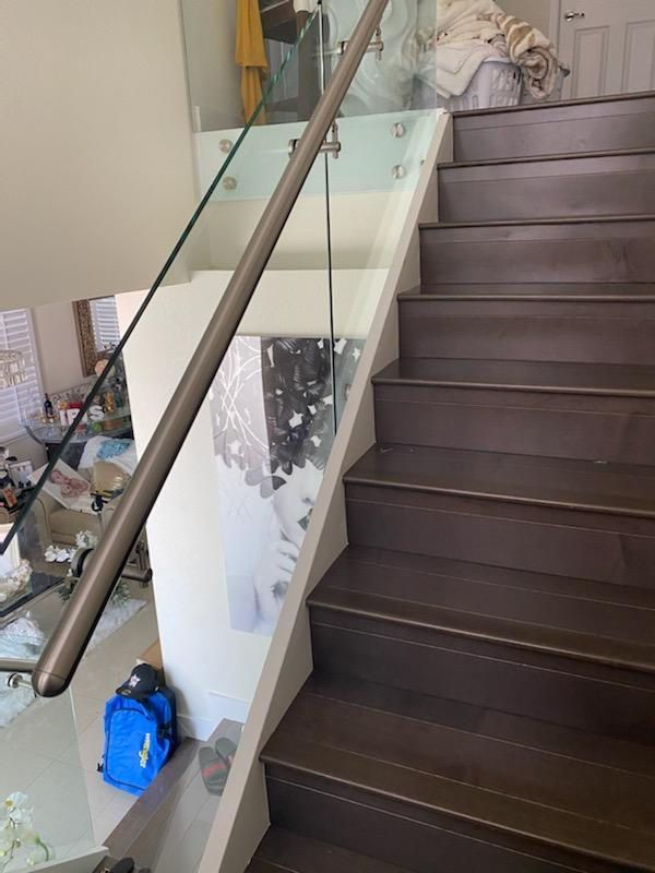 Wooden staircase with a glass railing and a silver handrail. Blue backpack on a ledge.