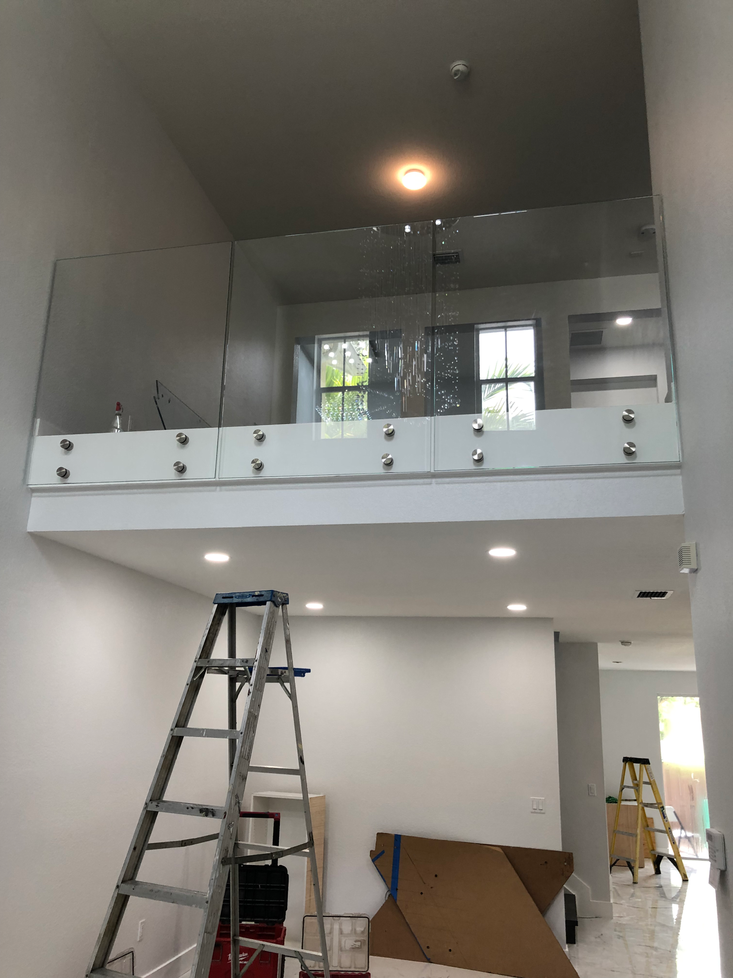 Interior view of a two-story space with a glass balcony railing and construction materials, including a ladder.