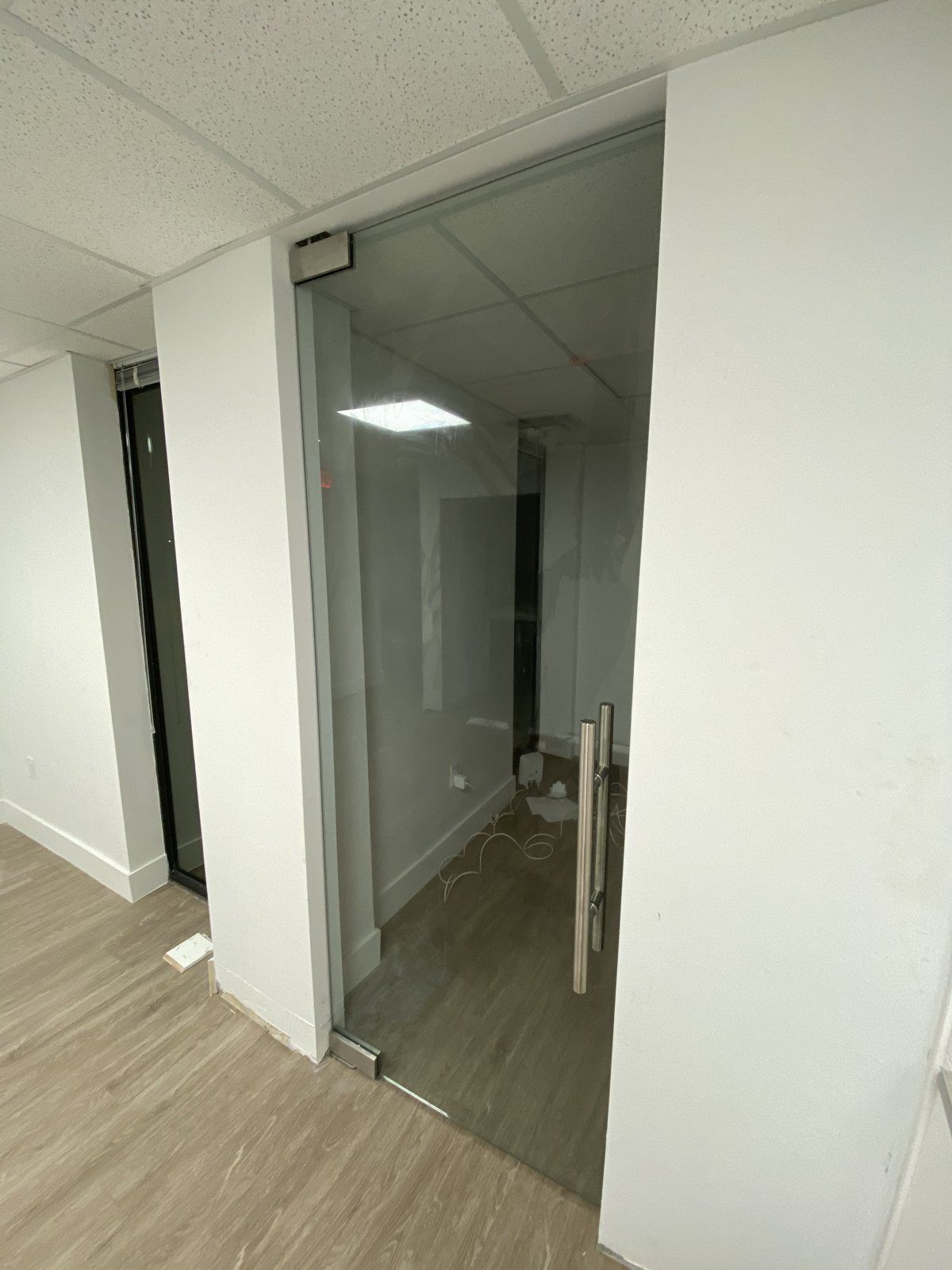 Entrada de oficina privada con panel de vidrio transparente sin marco y puerta abatible de vidrio en una abertura de drywall, Miami