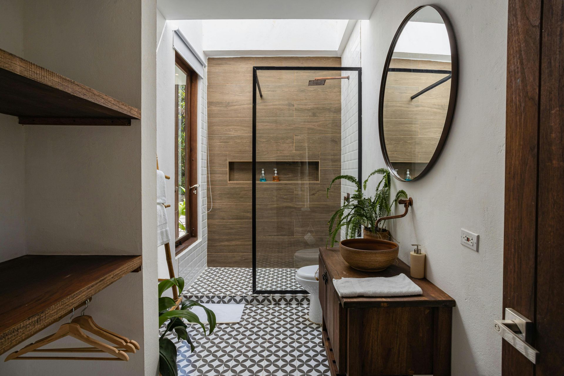 Bathroom with a wood vanity, large mirror, glass shower, and patterned tile floor.