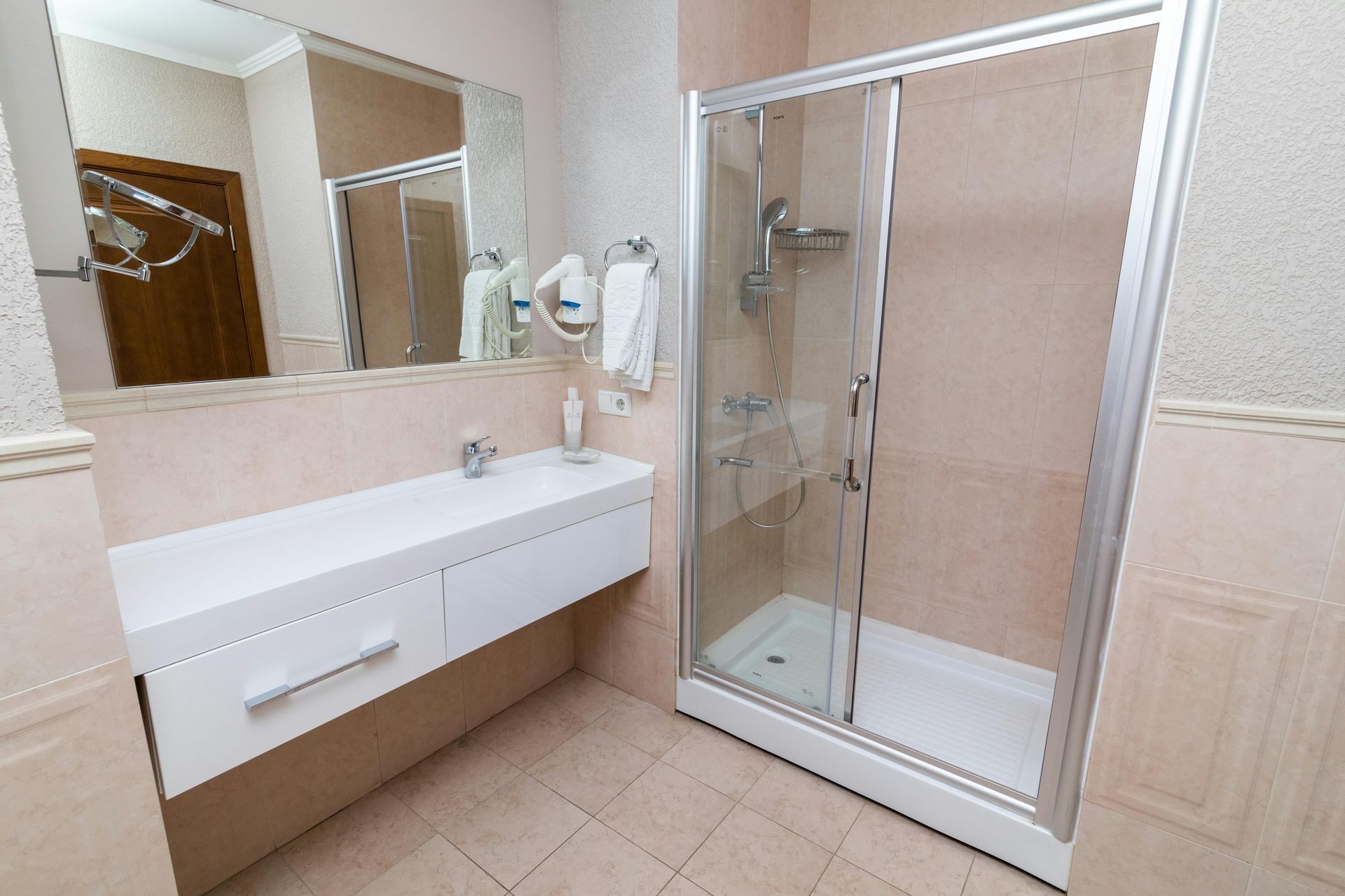 Bathroom with white vanity, shower, mirror, and beige tiled walls.