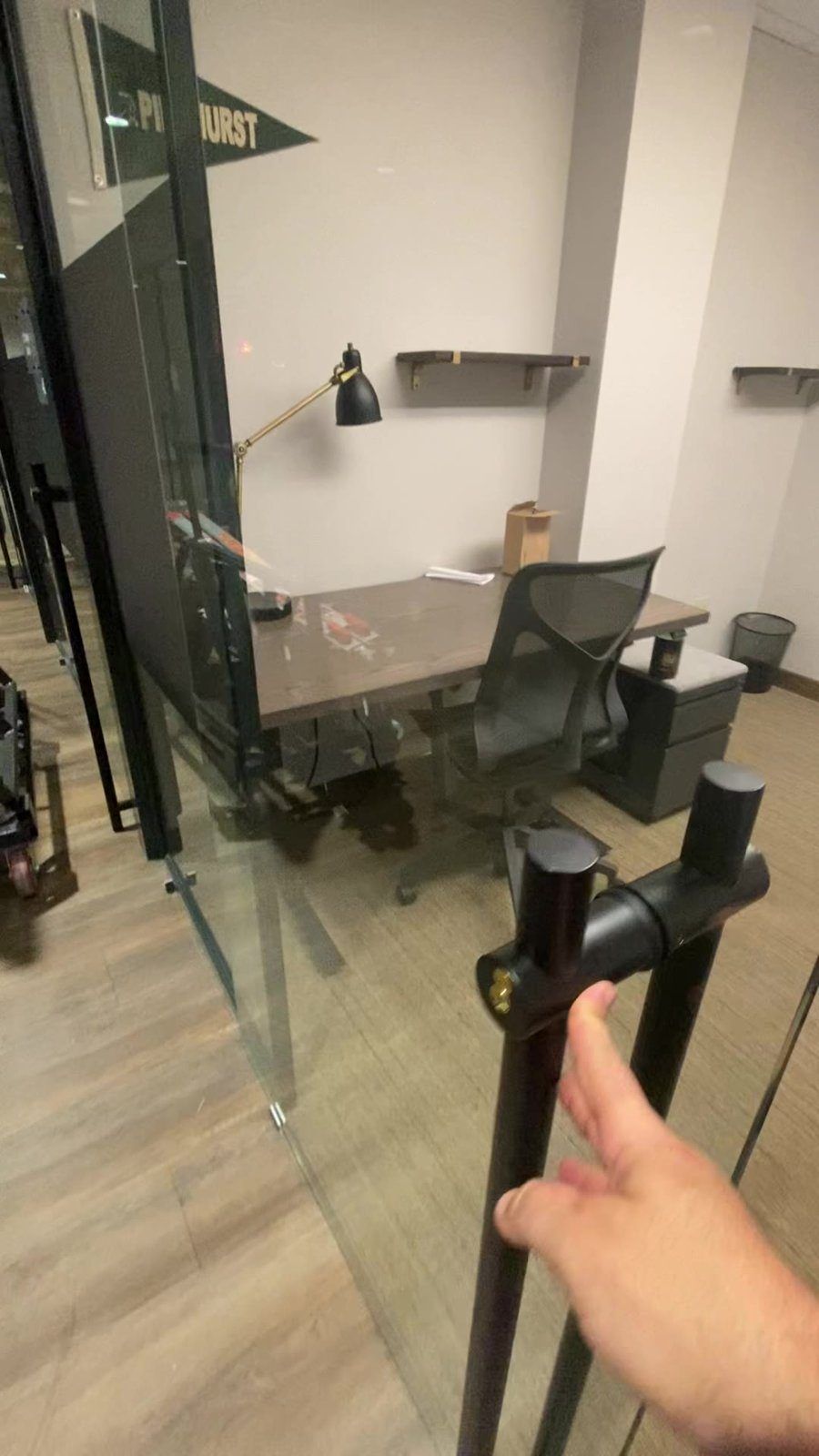 Mano abriendo una puerta de oficina de vidrio sin marco con tirador tipo escalera negro, con la oficina privada detrás del vidrio, Miami