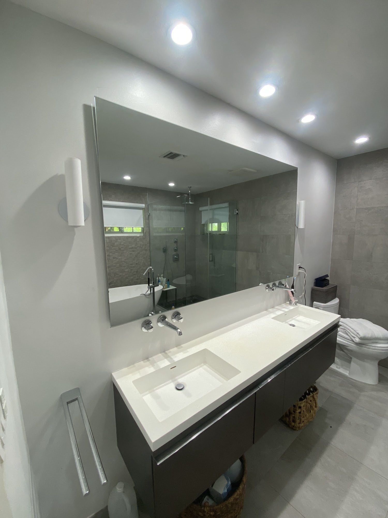 Mirror with internal lighting, mounted on ribbed wall above a dark sink and gold faucet.