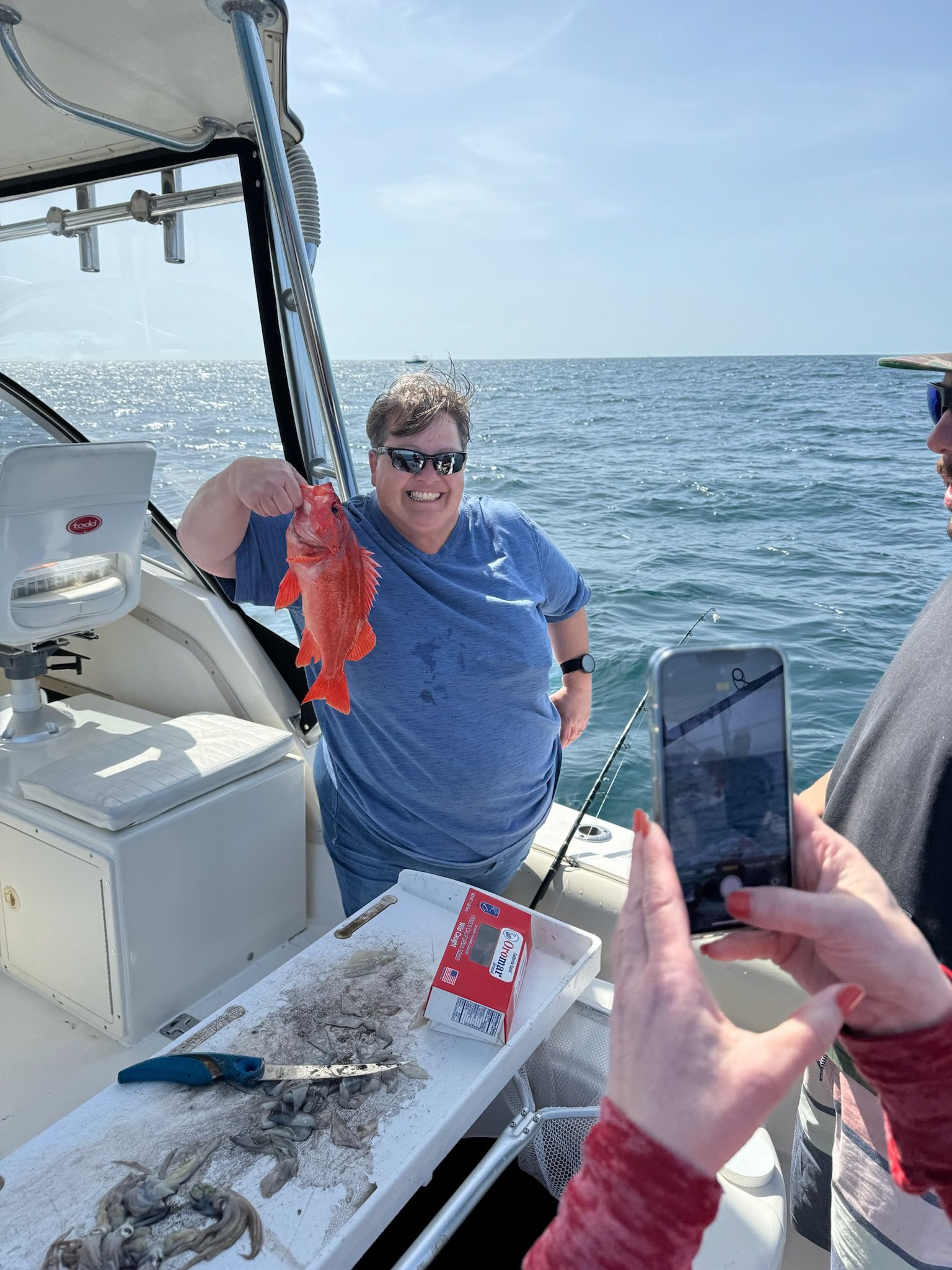 A man is taking a picture of a woman holding a fish on a boat.
