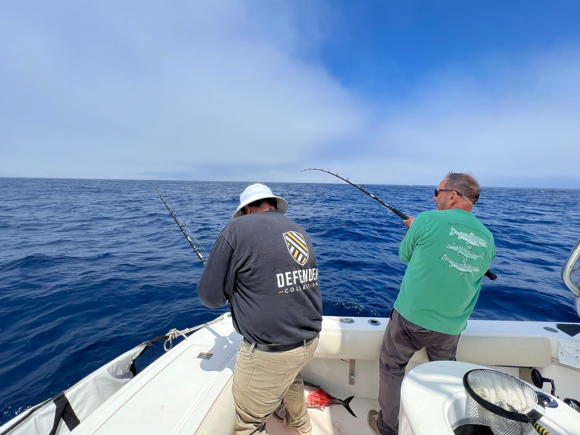 Two men are fishing on a boat in the ocean.