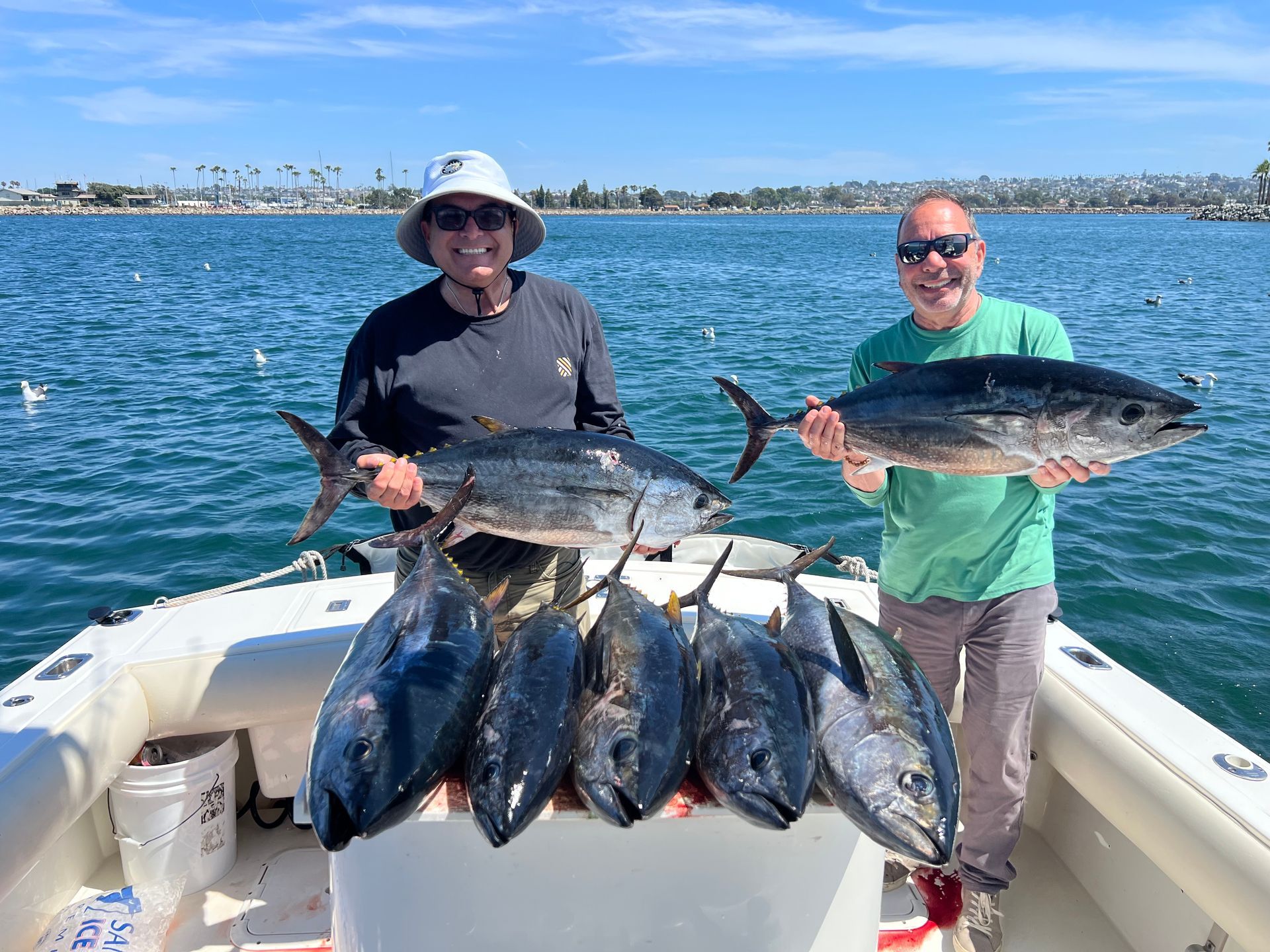 Two men are standing on a boat holding a bunch of fish.