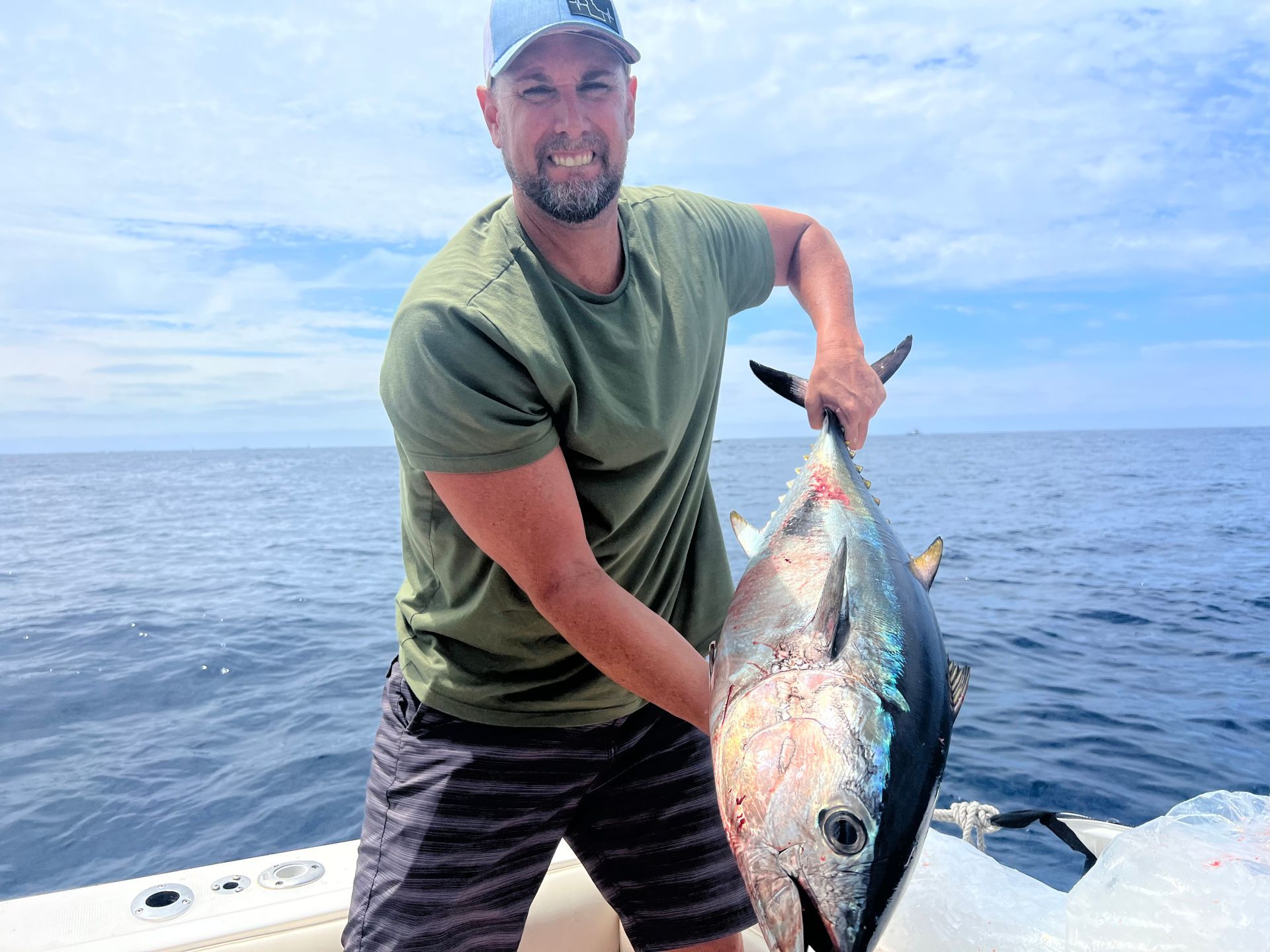 A man is holding a large fish on a boat in the ocean.