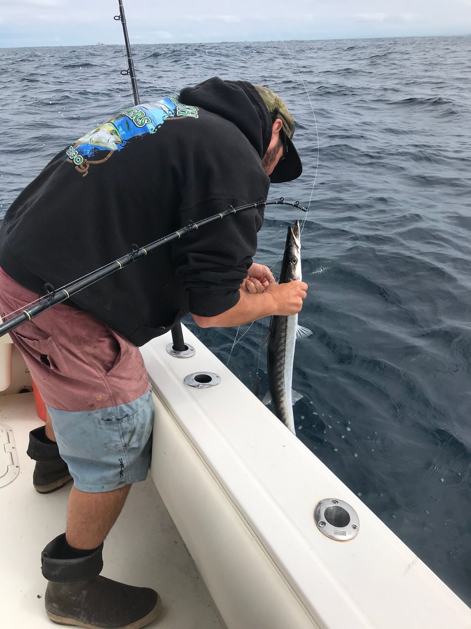 A man is fishing on a boat in the ocean while holding a fish.