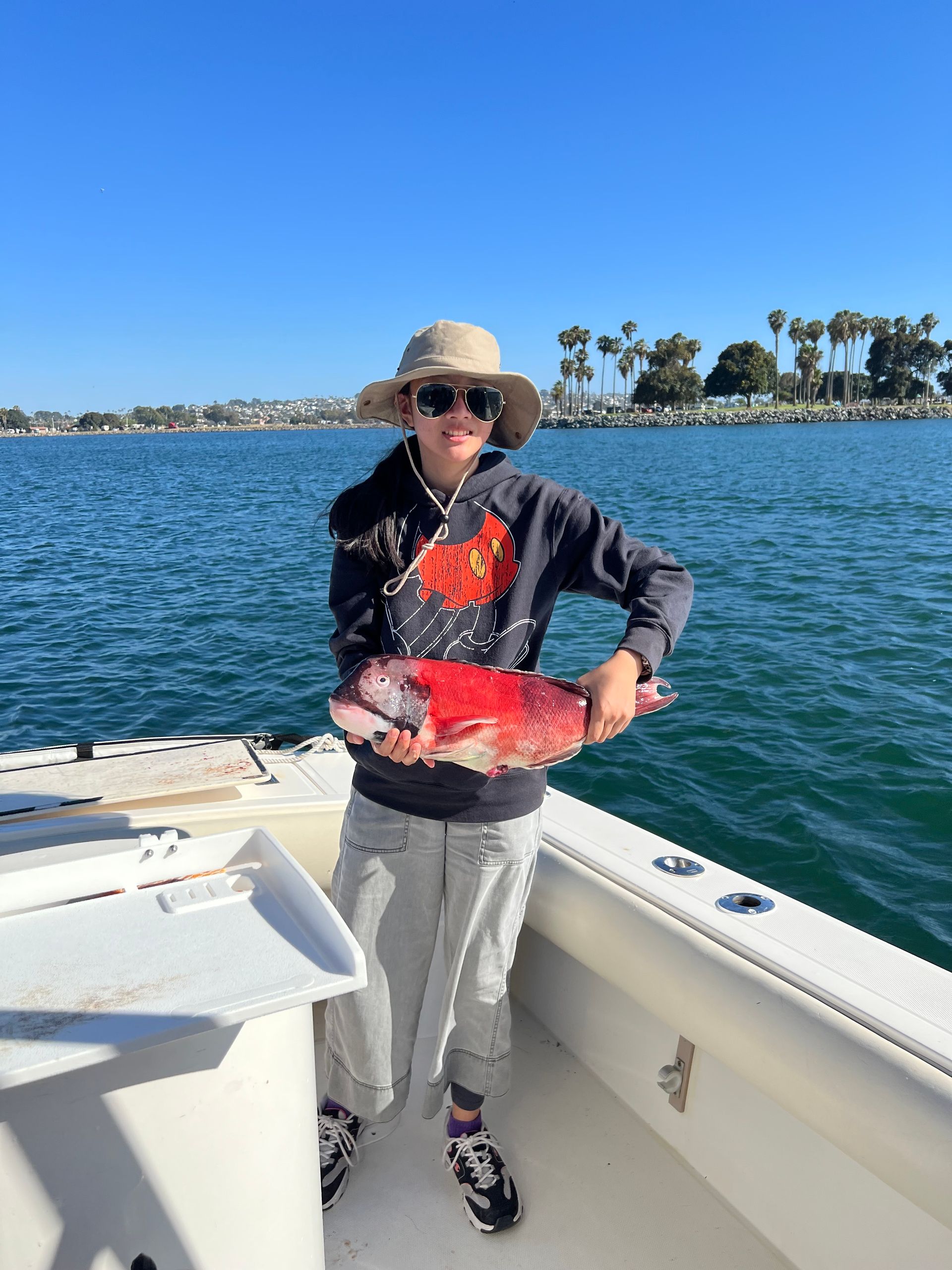 A woman is standing on a boat holding a large red fish.