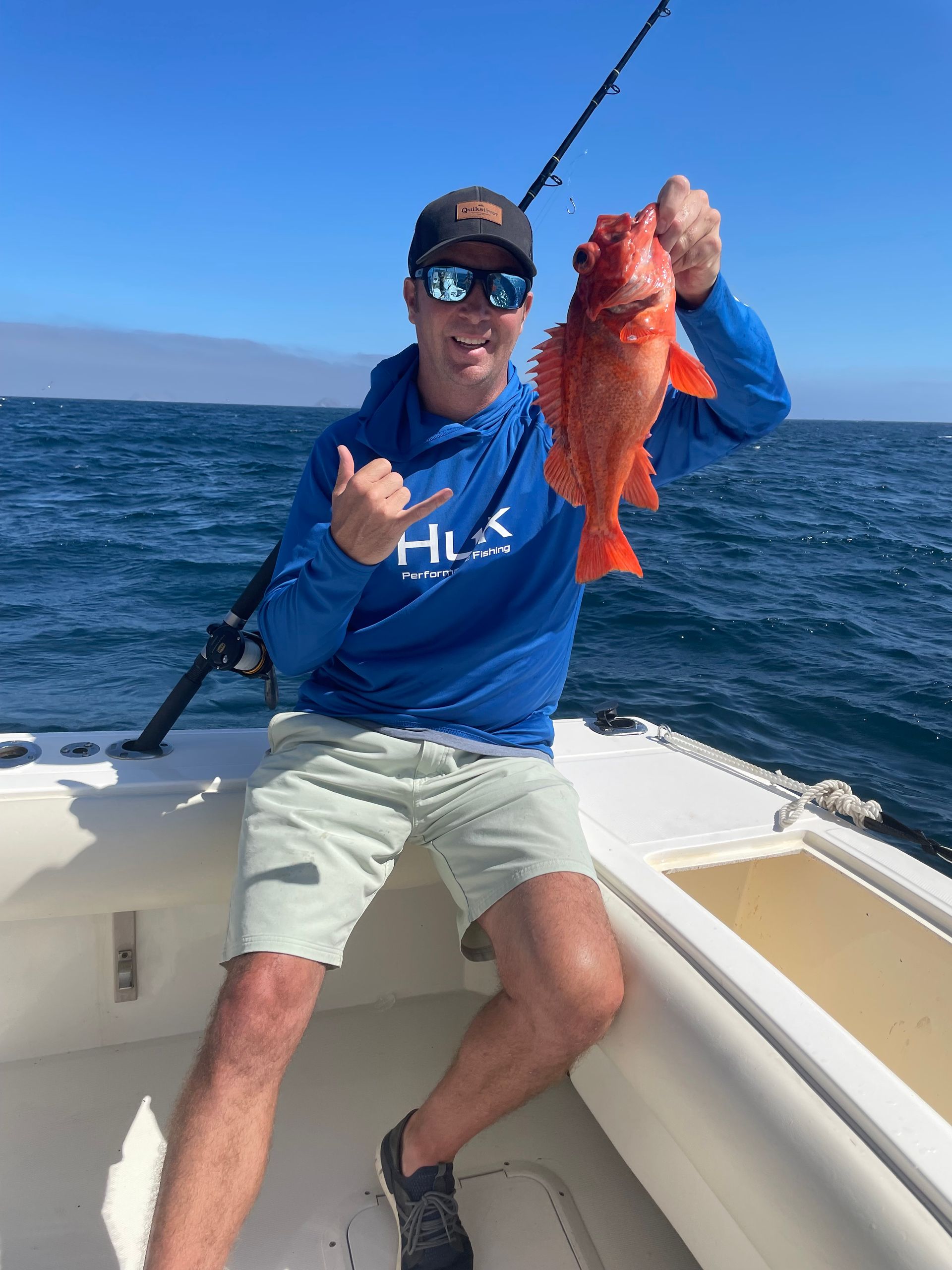 A man holding a fish on a boat with a blue shirt that says huk