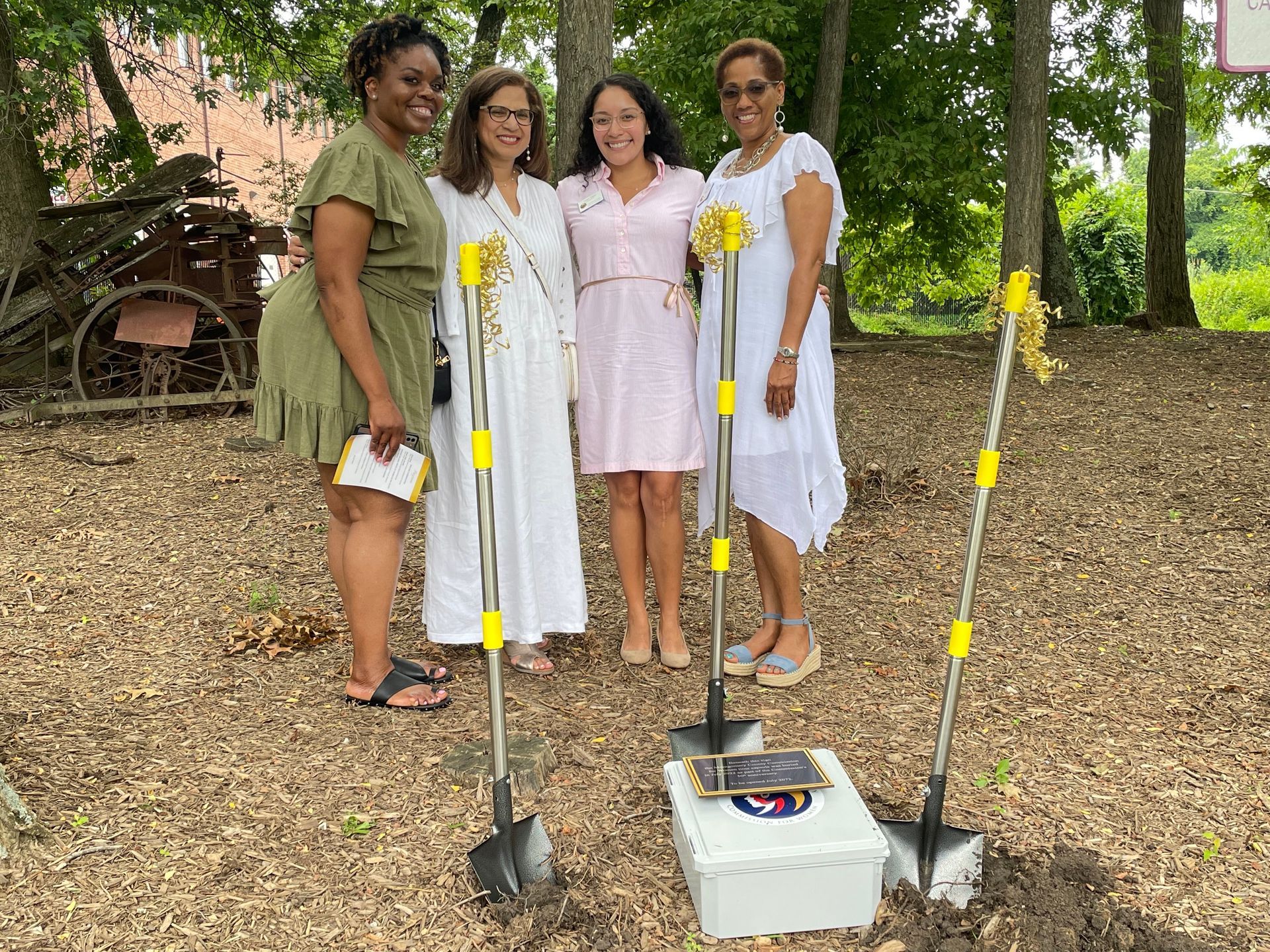 A group of women are standing next to shovels in a dirt field.