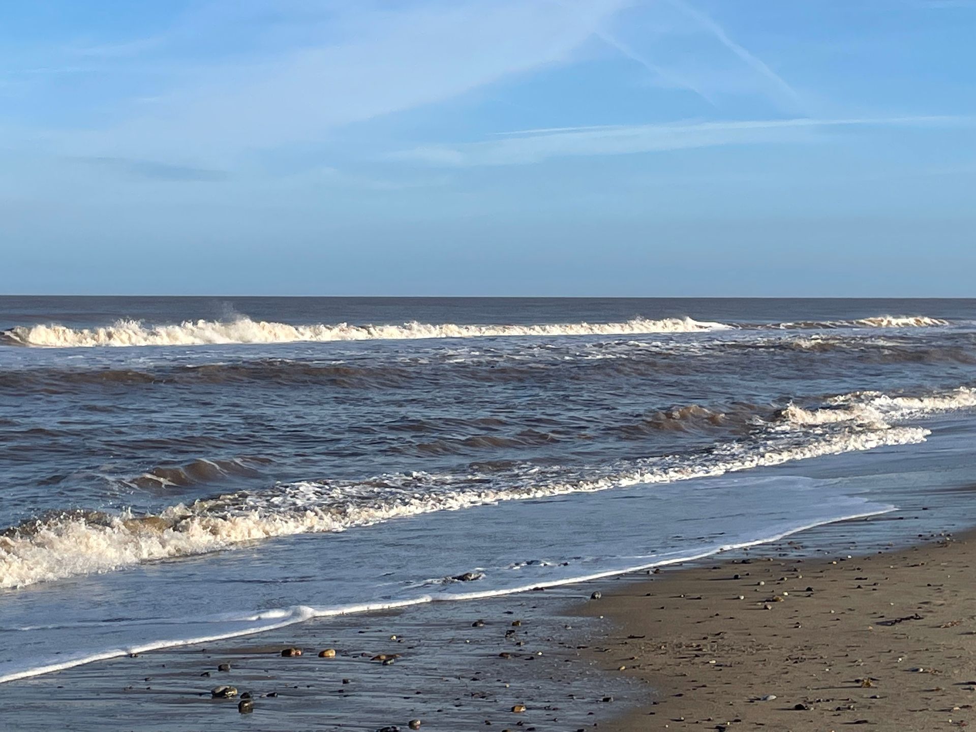 A beach with waves crashing against the shore on a sunny day.