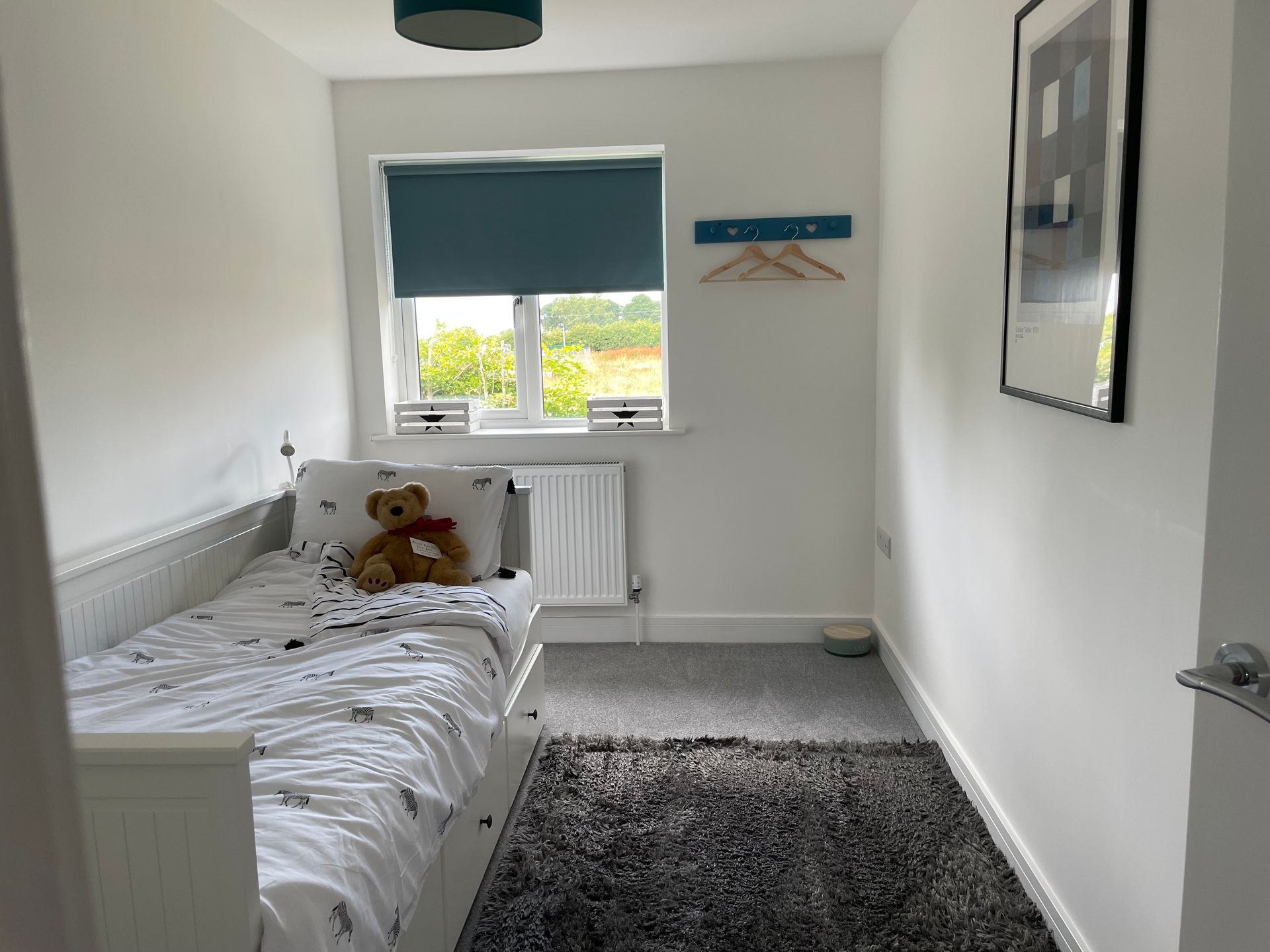 A small bedroom with a single bed and a teddy bear on the bed.