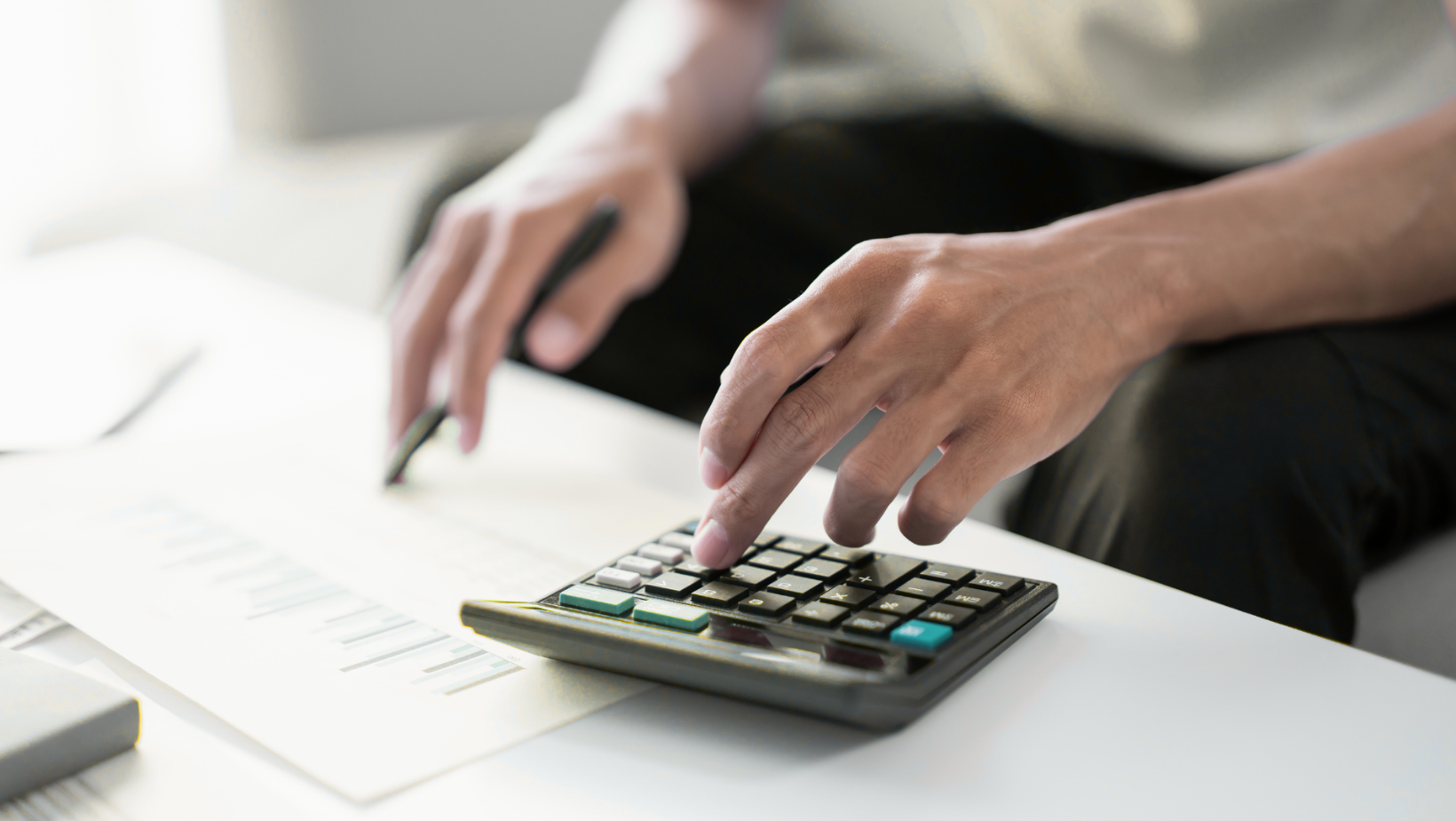 Hands using a calculator beside a document on a white desk
