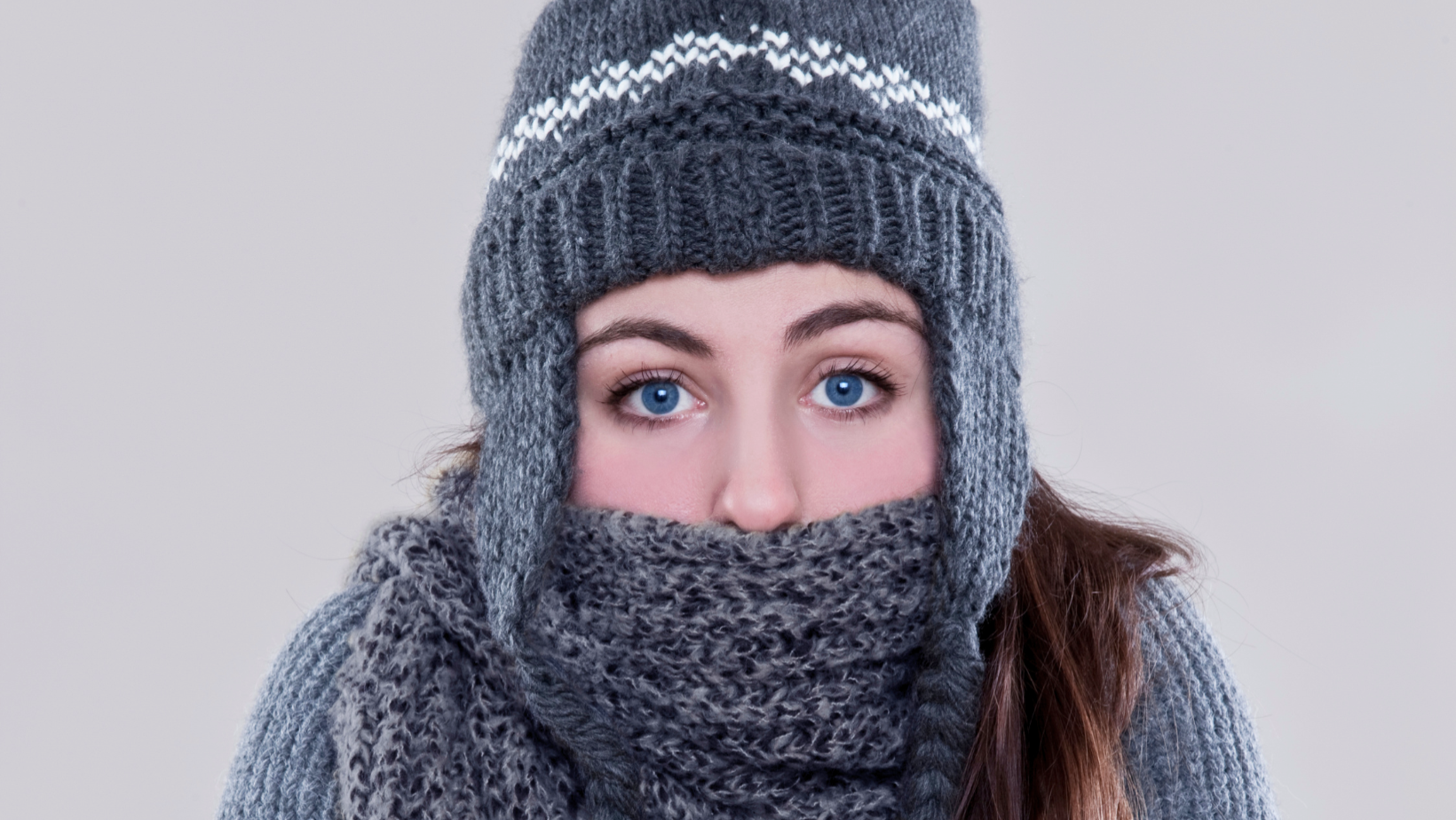 Woman wearing a gray knit hat and scarf, looking at the camera with only her eyes visible.