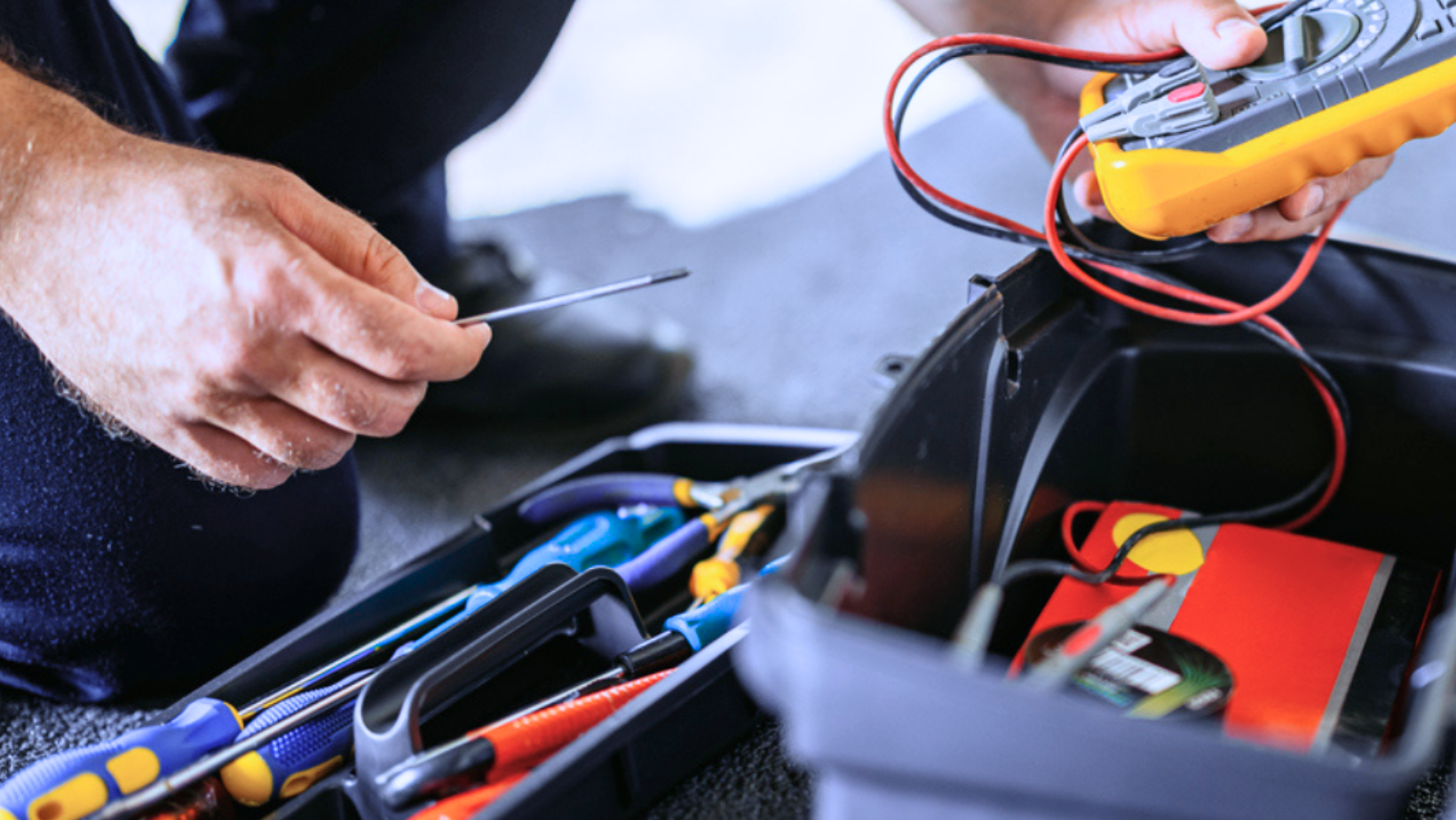 Technician using a multimeter to test wires in an open toolbox