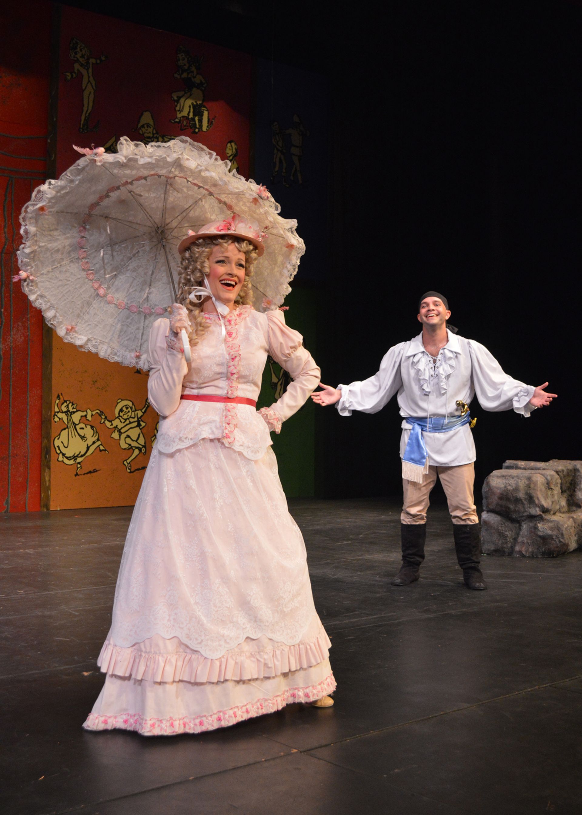 Two performers in period costumes on stage, one holding a white parasol, the other standing with arms open.