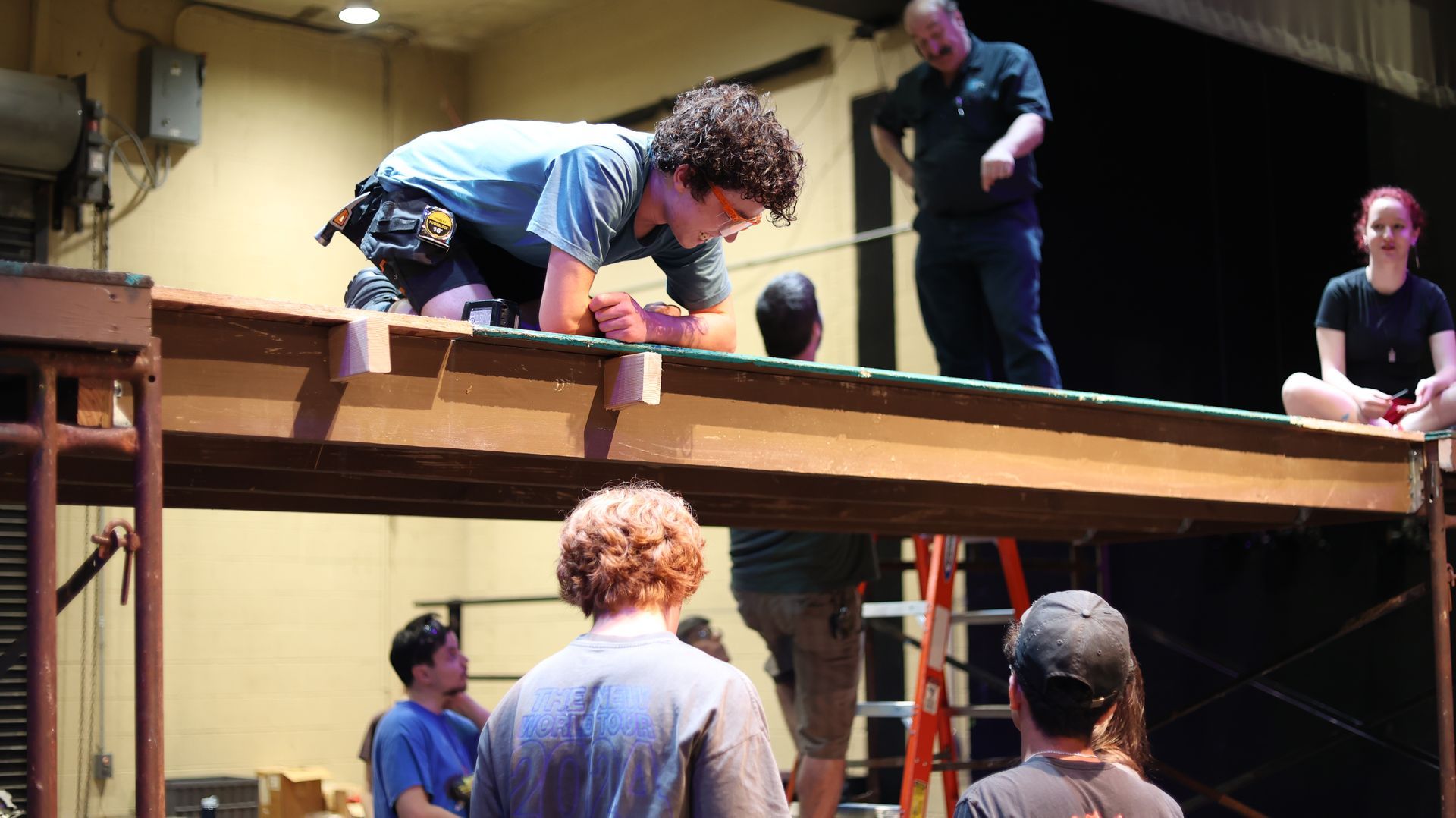 People performing on a wooden stage, with one crouching under warm indoor lighting.