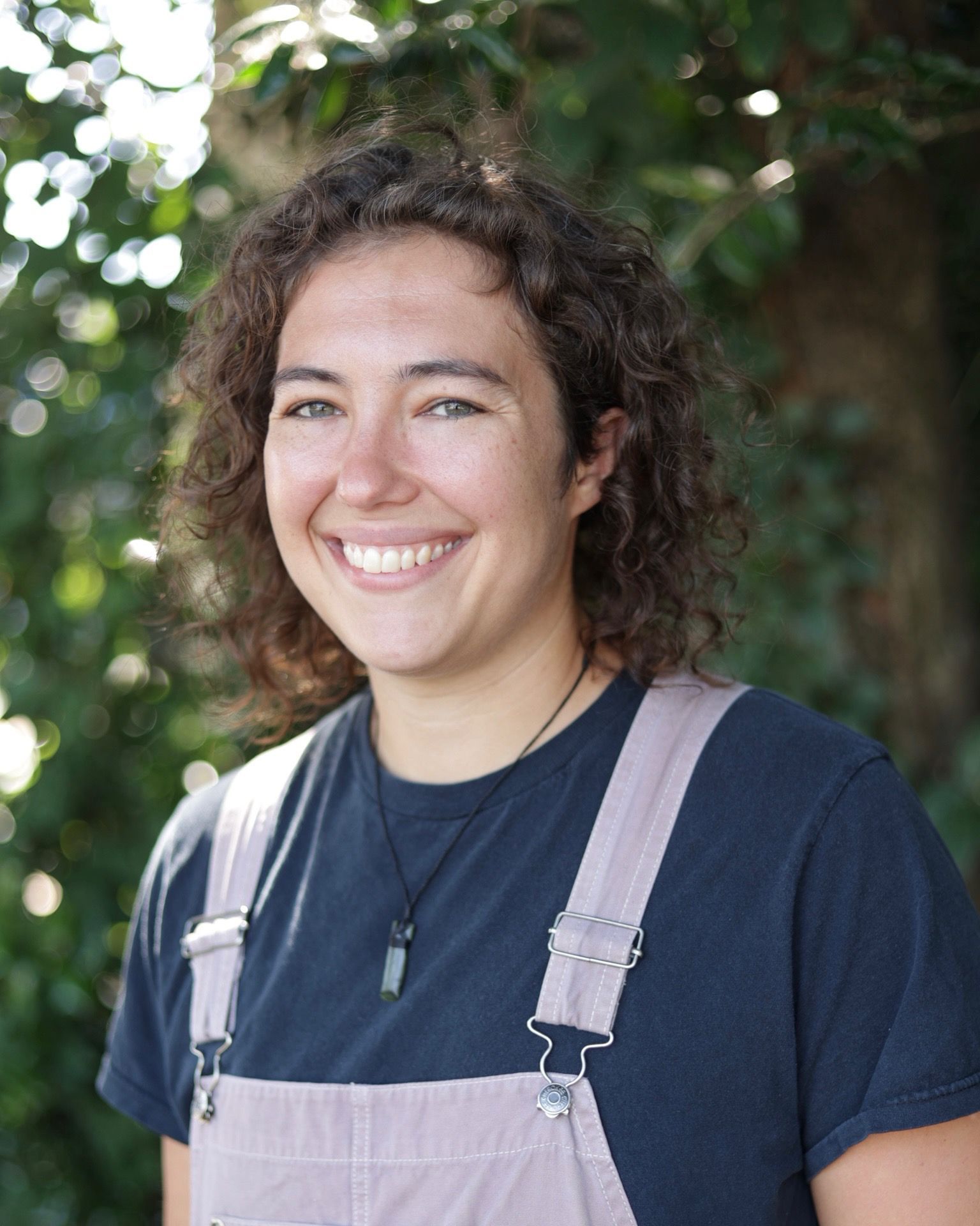 Smiling person in a black top standing before a brick wall.