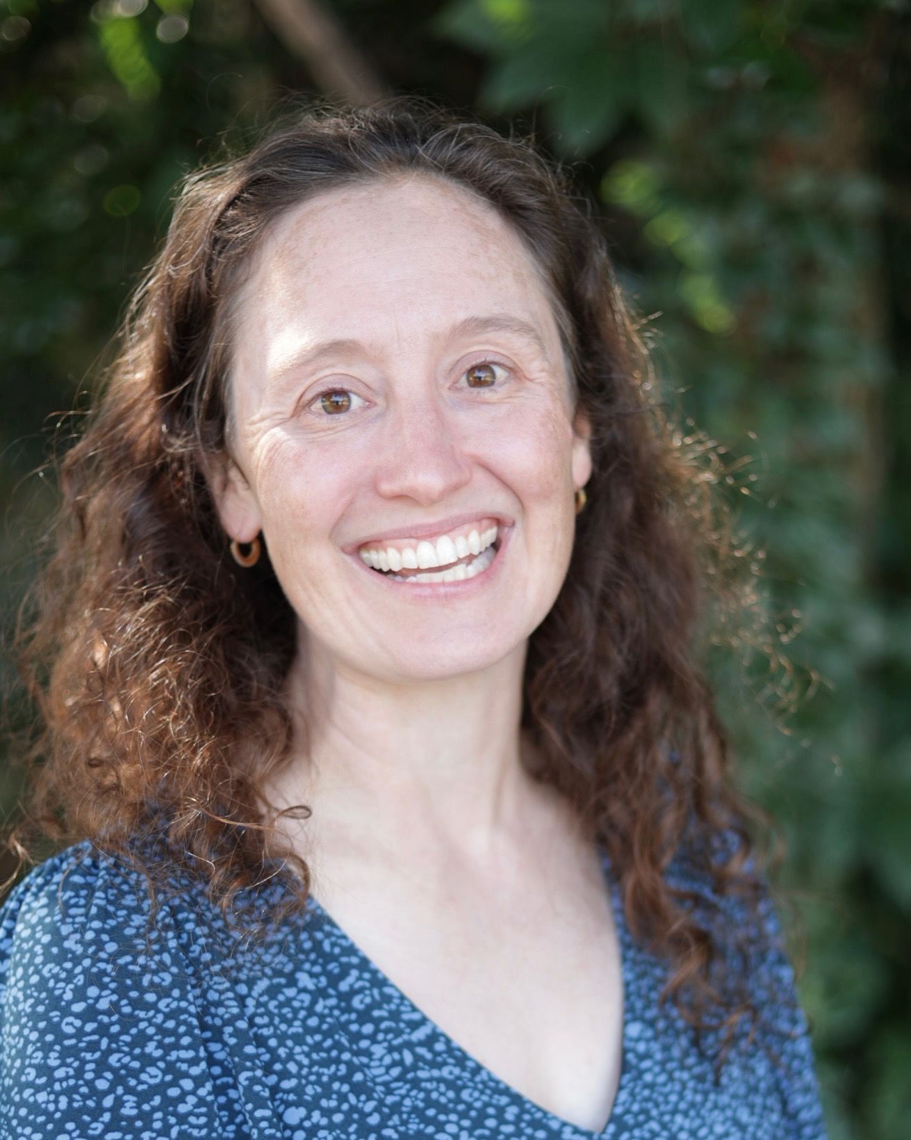 Smiling person with curly dark hair in a yellow sleeveless top against a teal background