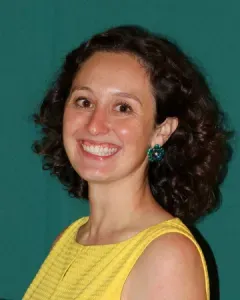 Smiling person with curly dark hair in a yellow sleeveless top against a teal background