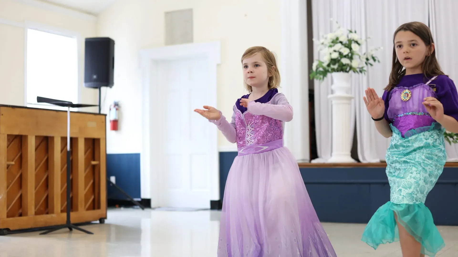 Two dancers in purple costumes performing on a bright indoor stage