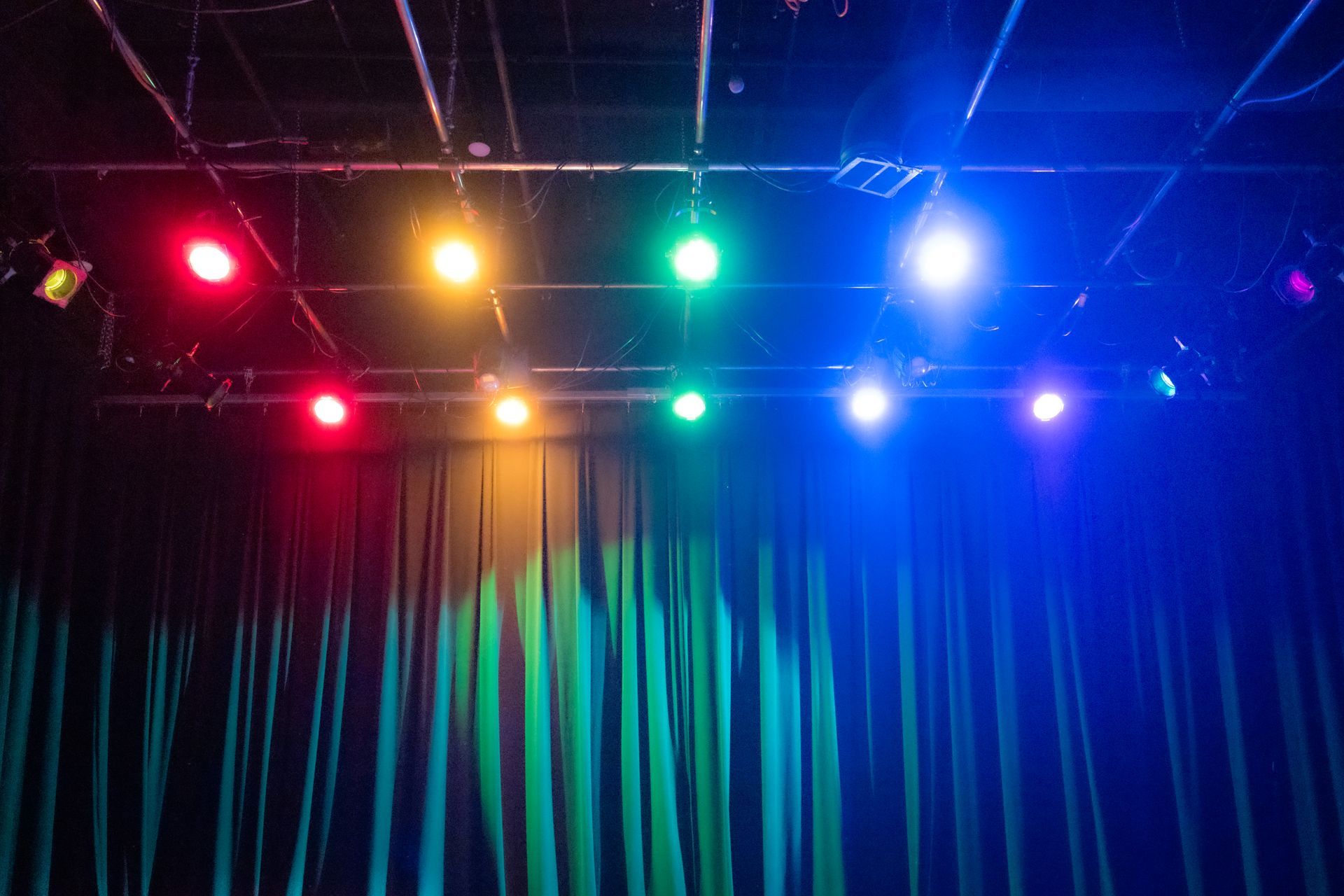 photo of black curtains with stage lights above shining red, yellow, green, blue and purple