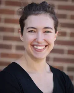 Smiling person in a black top standing before a brick wall.