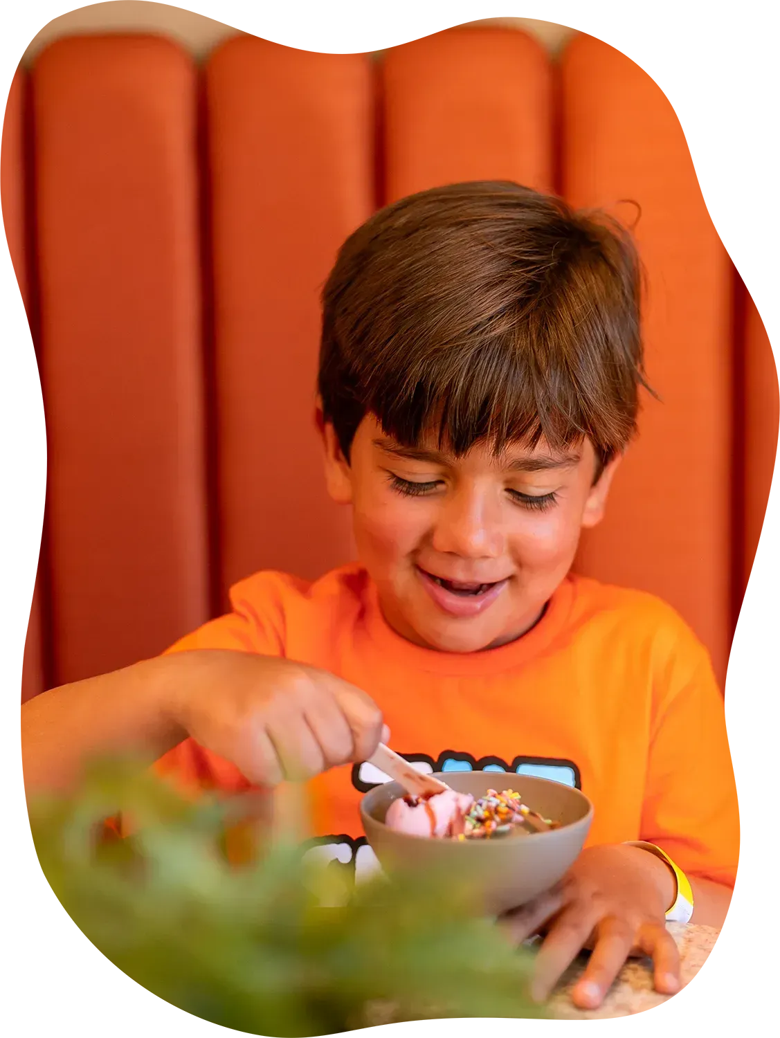 Um menino de camisa laranja está comendo cereal de uma tigela