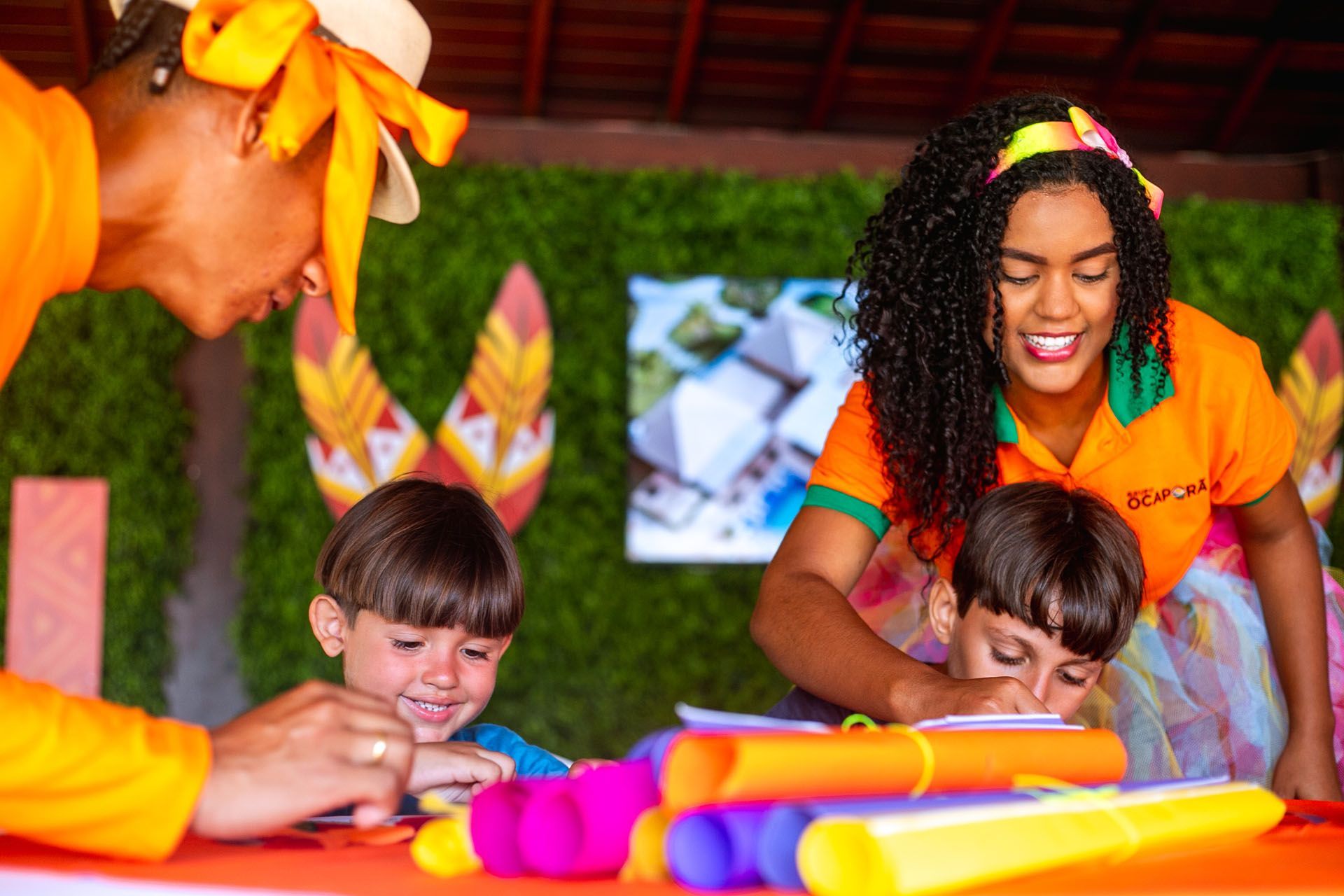 Uma mulher e duas crianças estão sentadas à mesa brincando com brinquedos.
