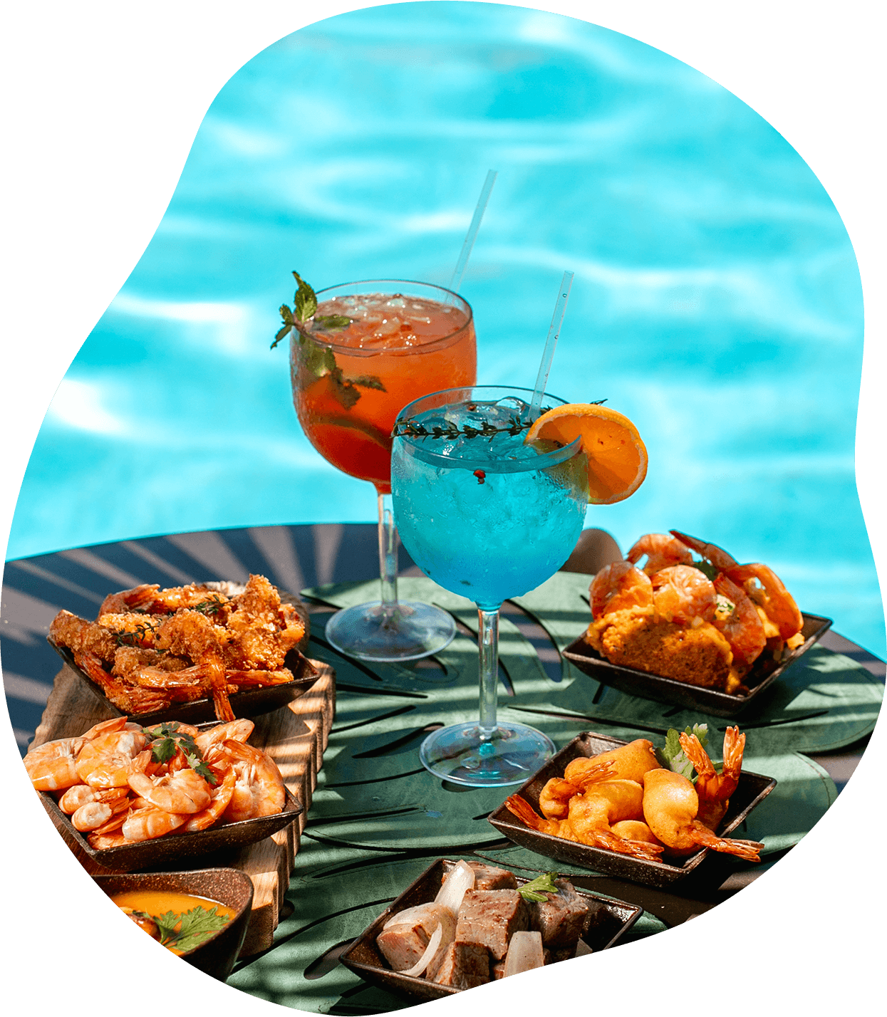 Uma mesa com comida e bebidas ao lado de uma piscina.