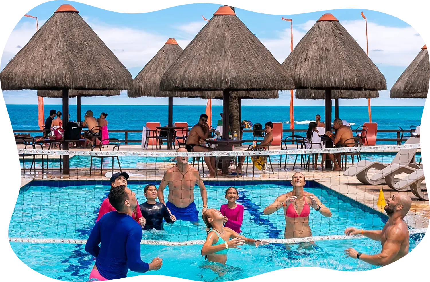 Um grupo de pessoas está brincando em uma piscina com guarda-sóis de palha.
