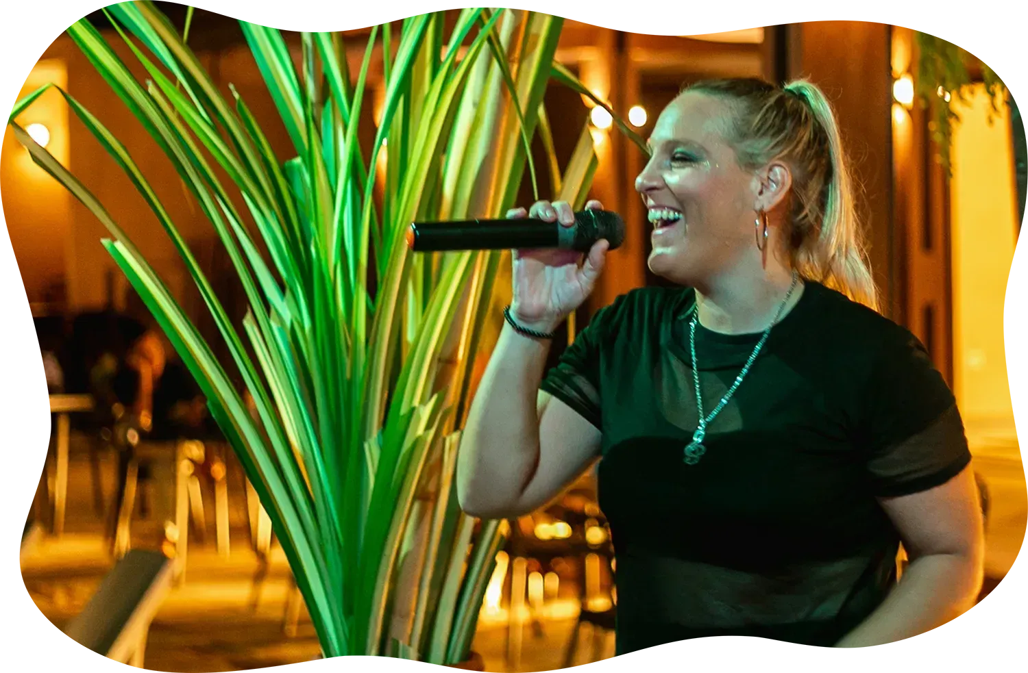 Uma mulher está cantando em um microfone em frente a uma planta.