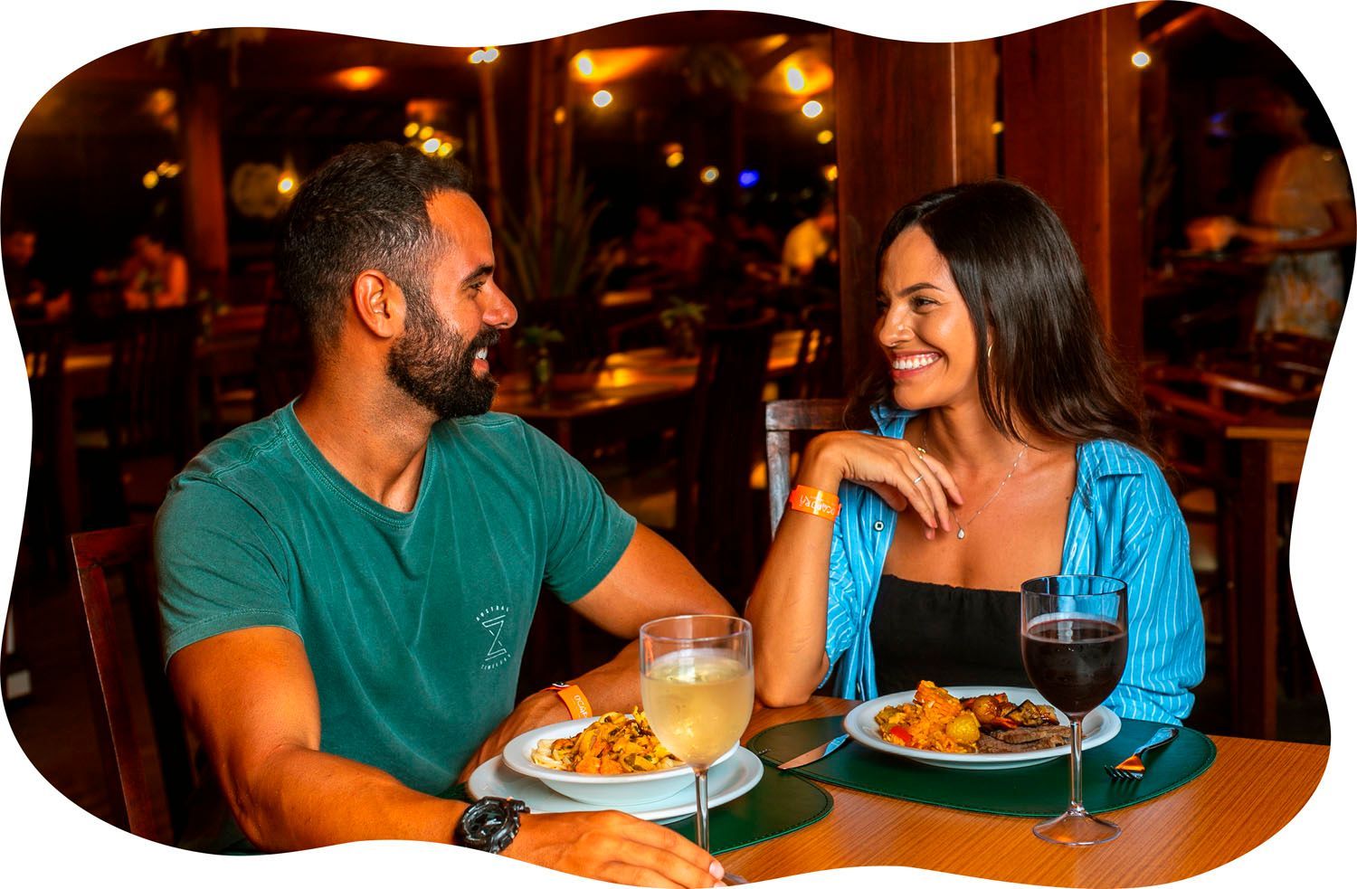 Um homem e uma mulher estão sentados à mesa com pratos de comida e taças de vinho.