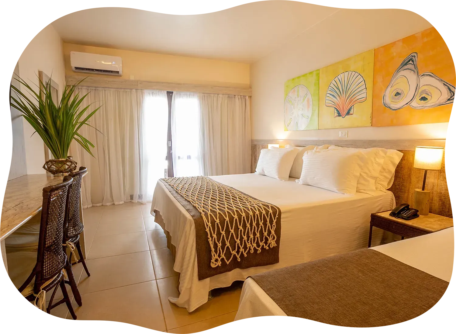 Um quarto de hotel com uma cama, escrivaninha, cadeiras e pinturas na parede.