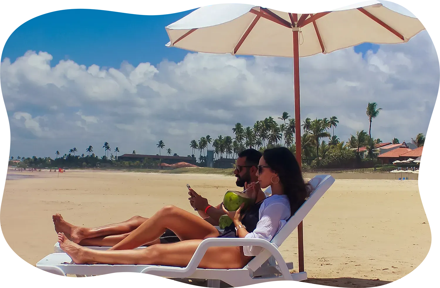 Um homem e uma mulher estão deitados na praia sob um guarda-chuva