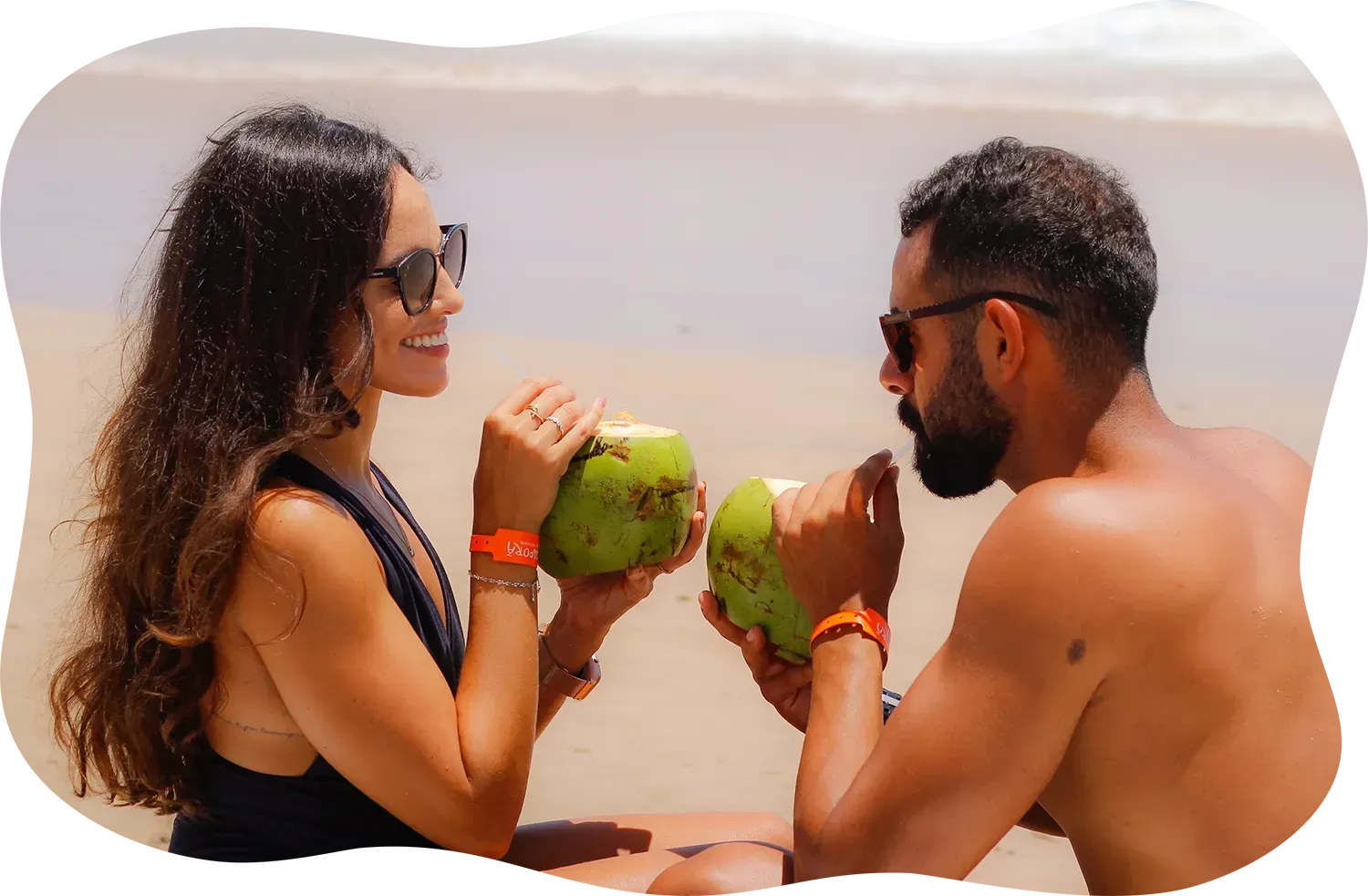 Um homem e uma mulher estão bebendo água de coco na praia.