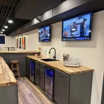 A modern, open-concept kitchen with grey cabinets, stainless steel appliances, and a small dining table on wood floors.