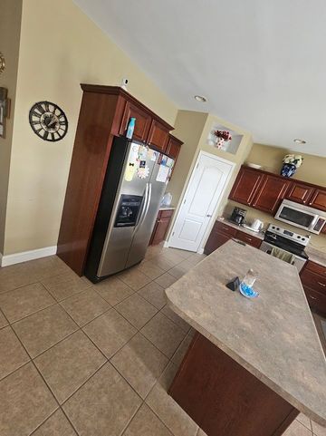 A kitchen with sage green walls, white cabinets, stainless steel appliances, and a central step ladder on wood flooring.