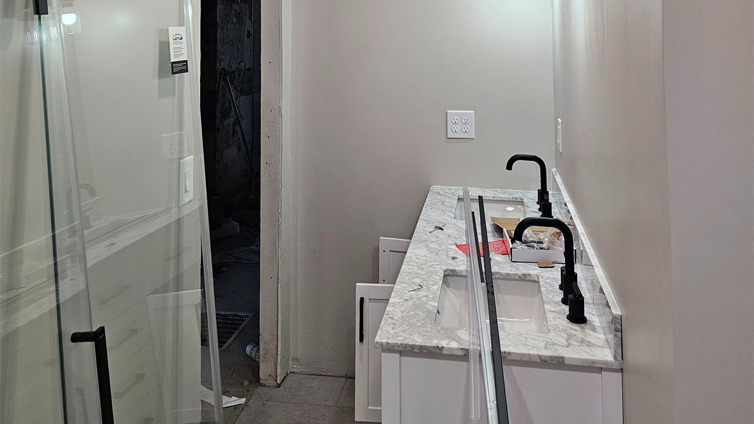 Narrow bathroom with a glass shower, sink cabinet, and tools on the countertop during renovation.