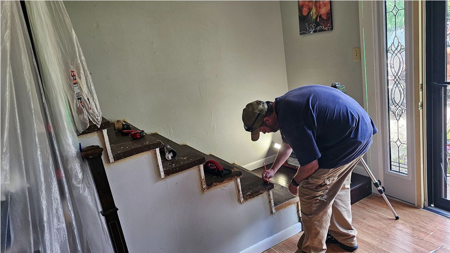 Person painting the trim on a staircase inside a home, using a small brush near the steps.