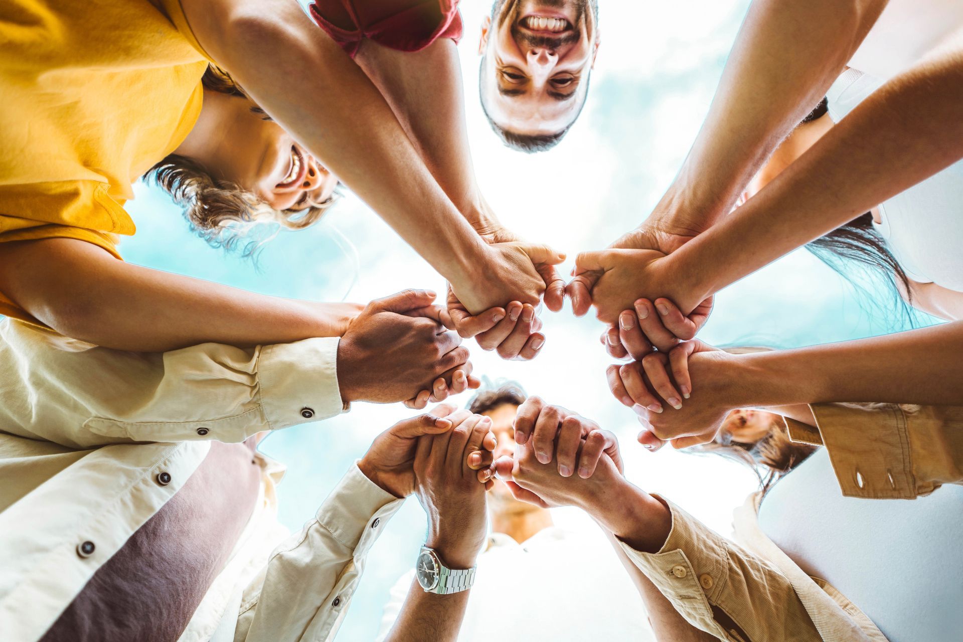 People stacking hands in a circle against a bright blue sky