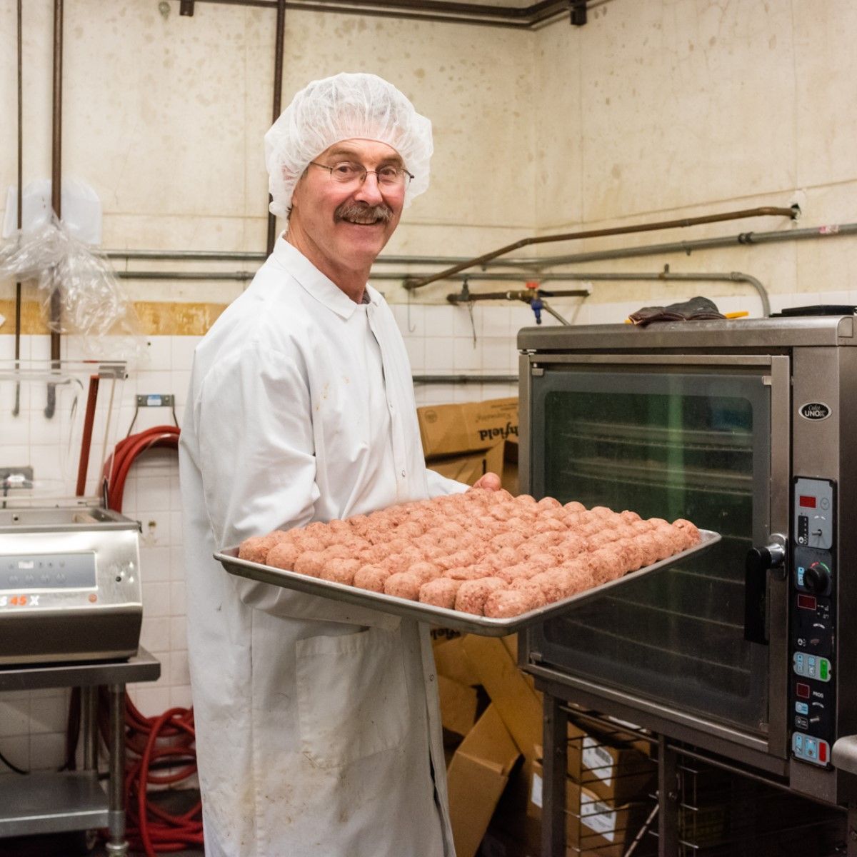 A man holding a tray of meatballs in a kitchen
